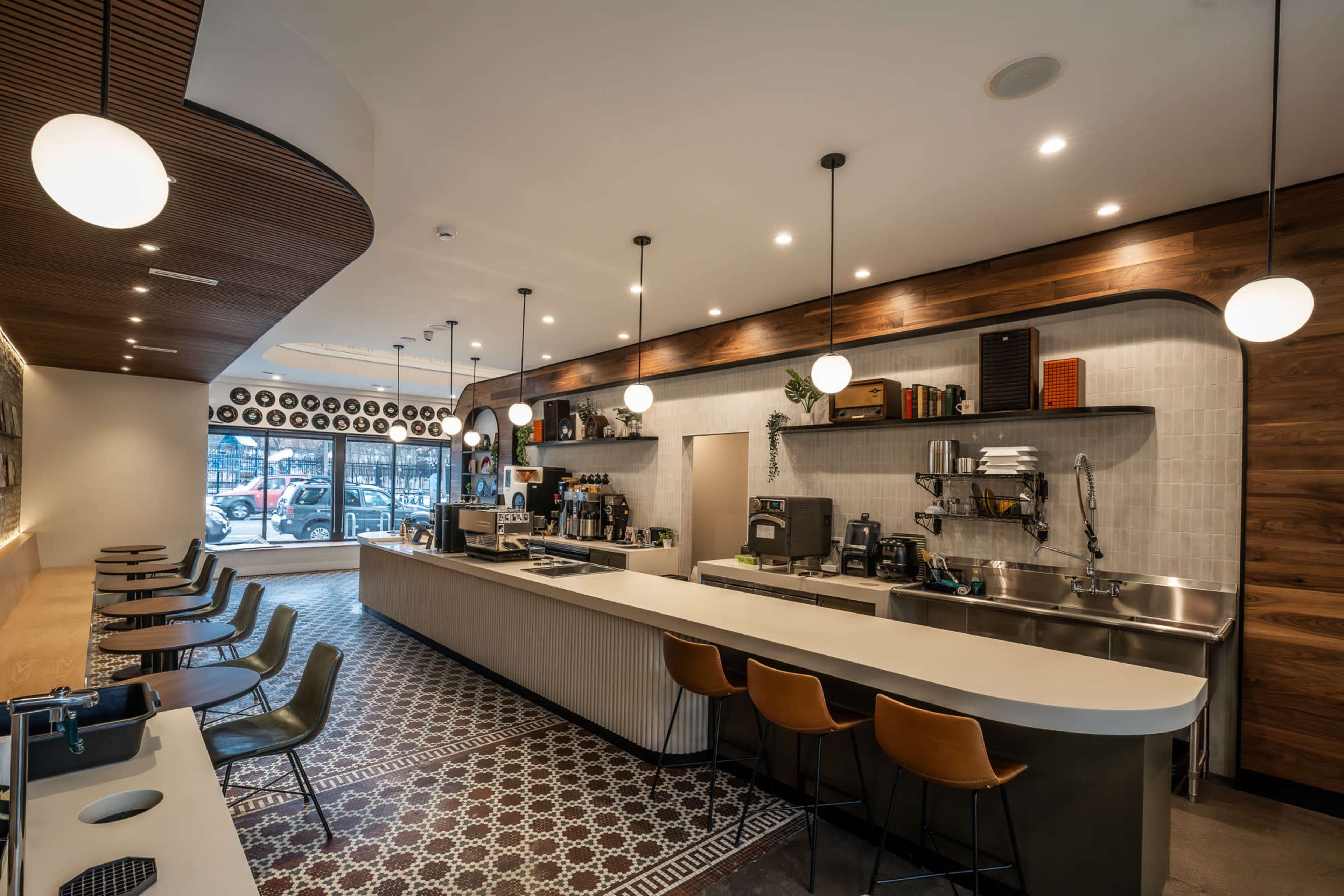 The image shows a modern café interior featuring a long counter with seating and stylish light fixtures.