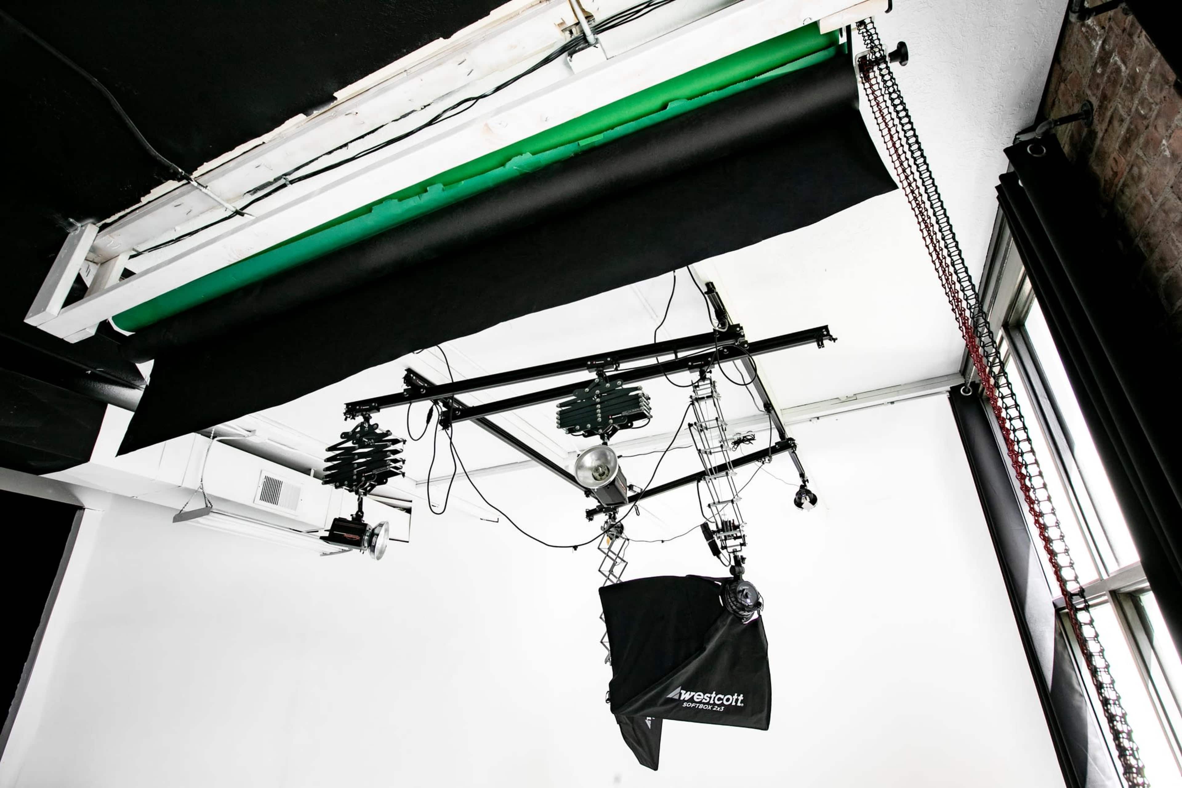 A photography studio setup with various lighting equipment and a black backdrop suspended from the ceiling.