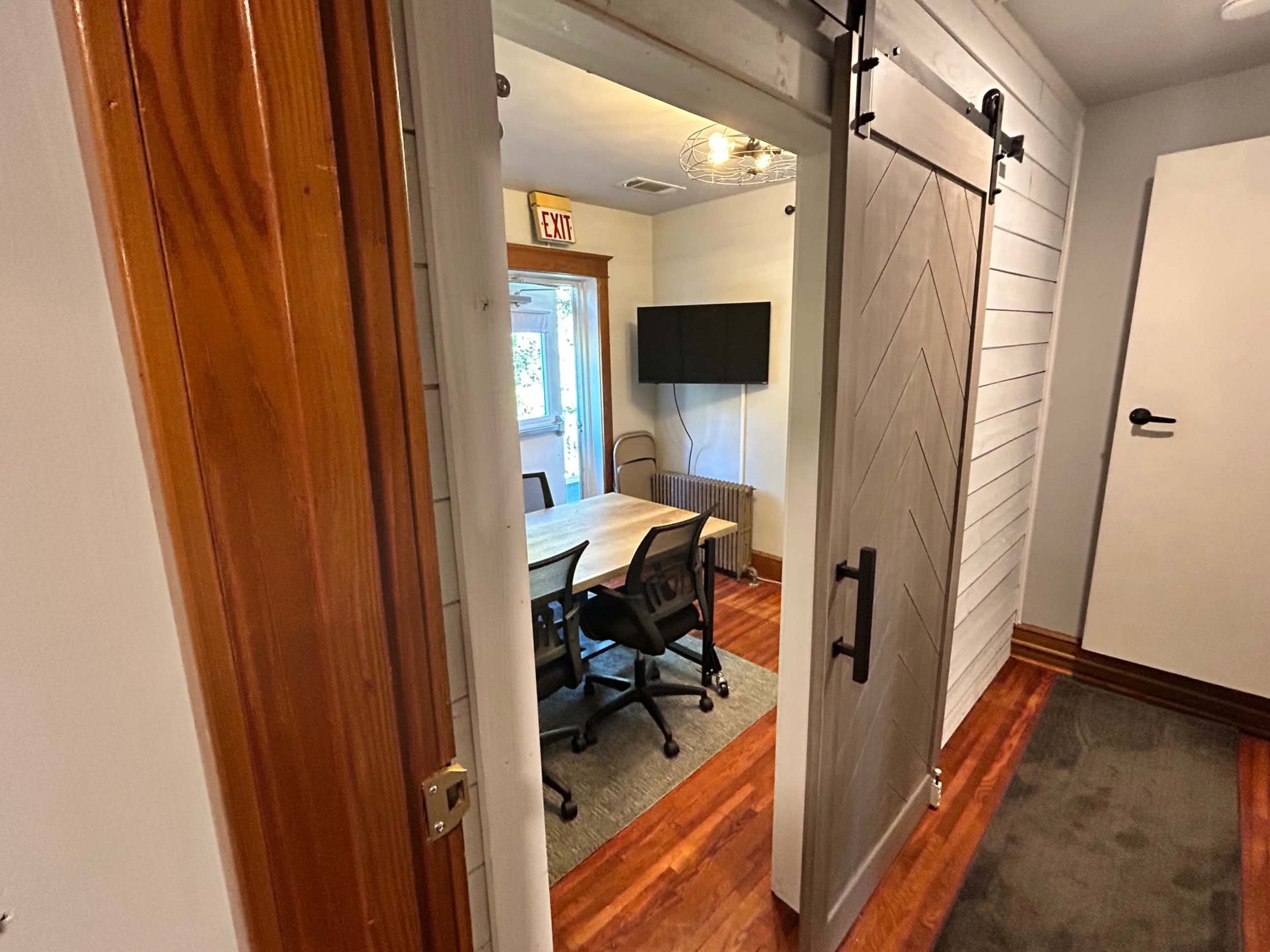 A view of a doorway leading into a conference room with a table and chairs, featuring a television mounted on the wall.