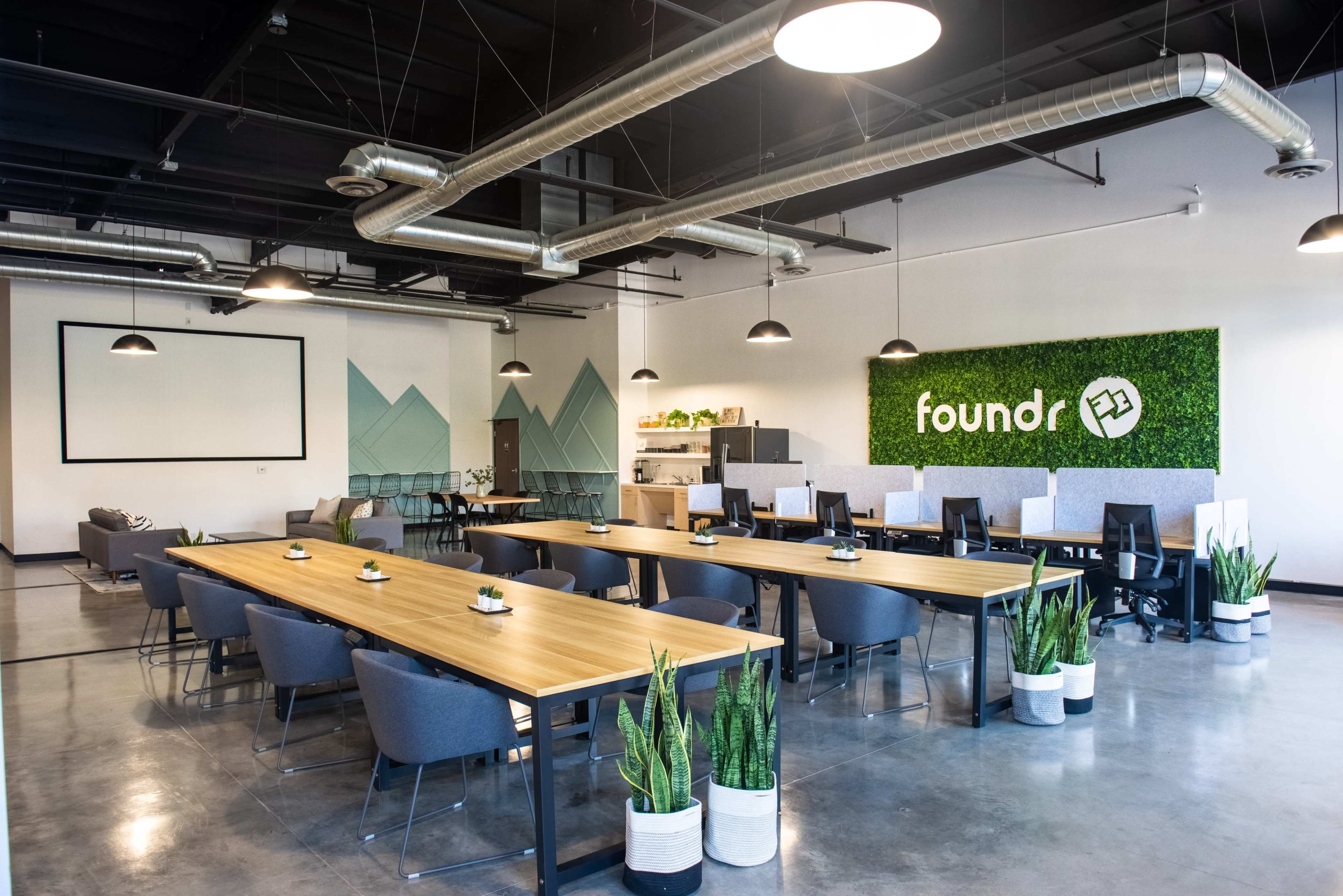 A modern office space features long wooden tables, gray chairs, and a greenery wall with the logo "foundr" prominently displayed.