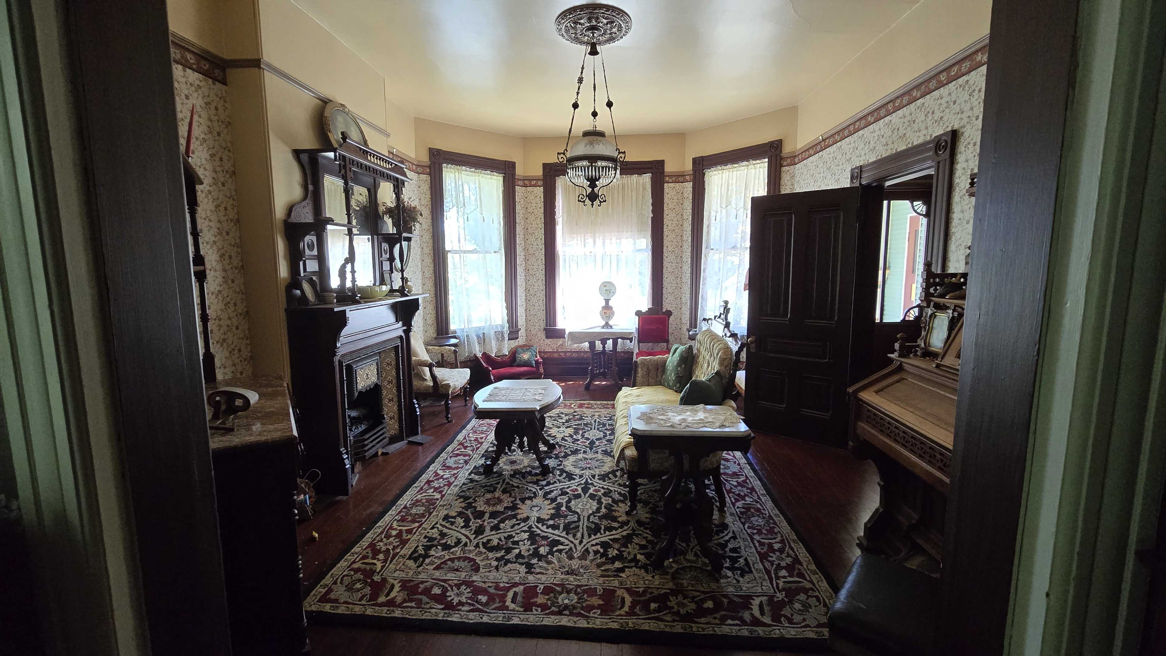 A Victorian-style living room with ornate furnishings, large windows, and decorative wallpaper.