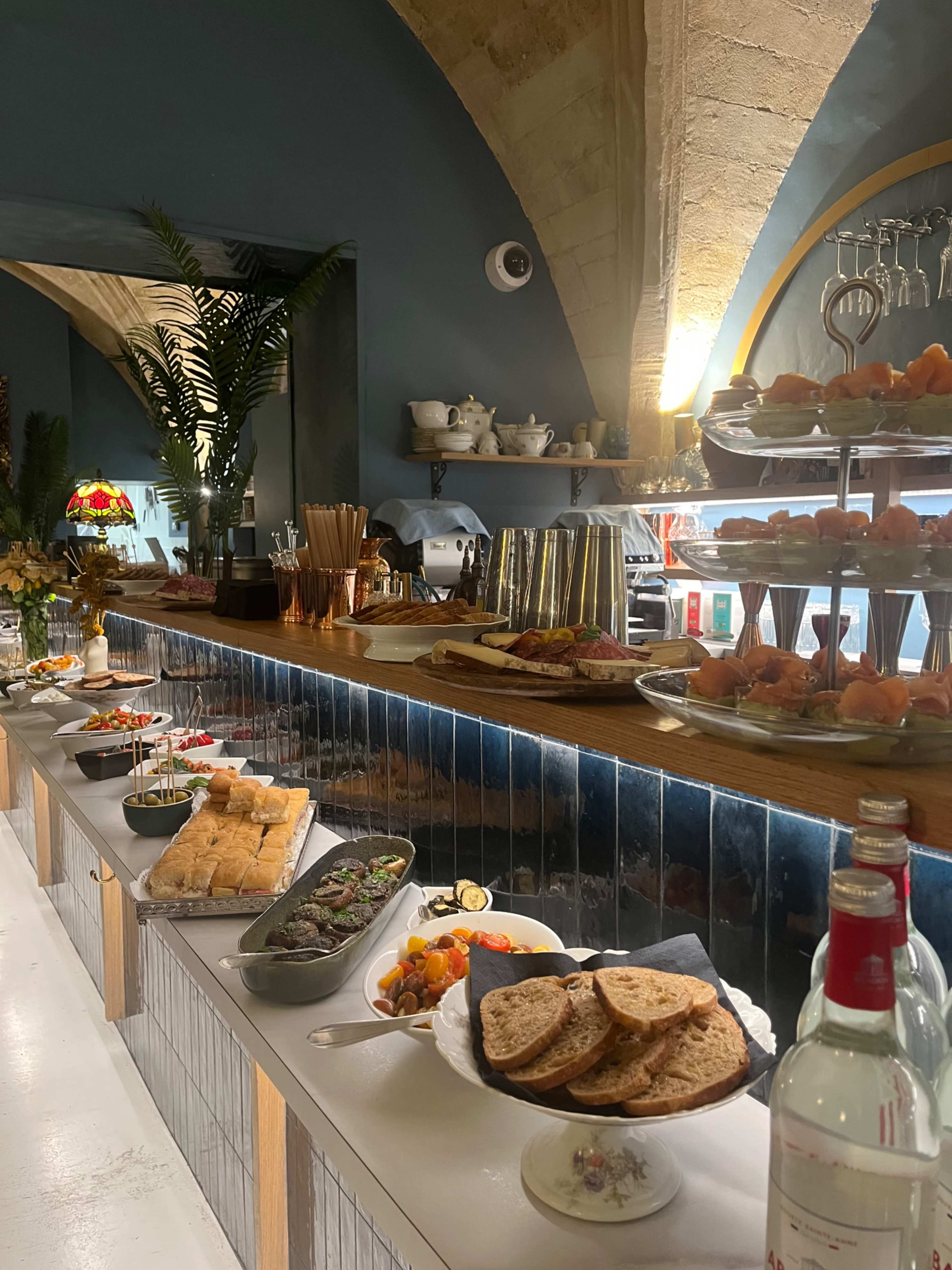 A long, wooden buffet table displays a variety of dishes and beverages in a restaurant with arched ceilings and decorative elements.