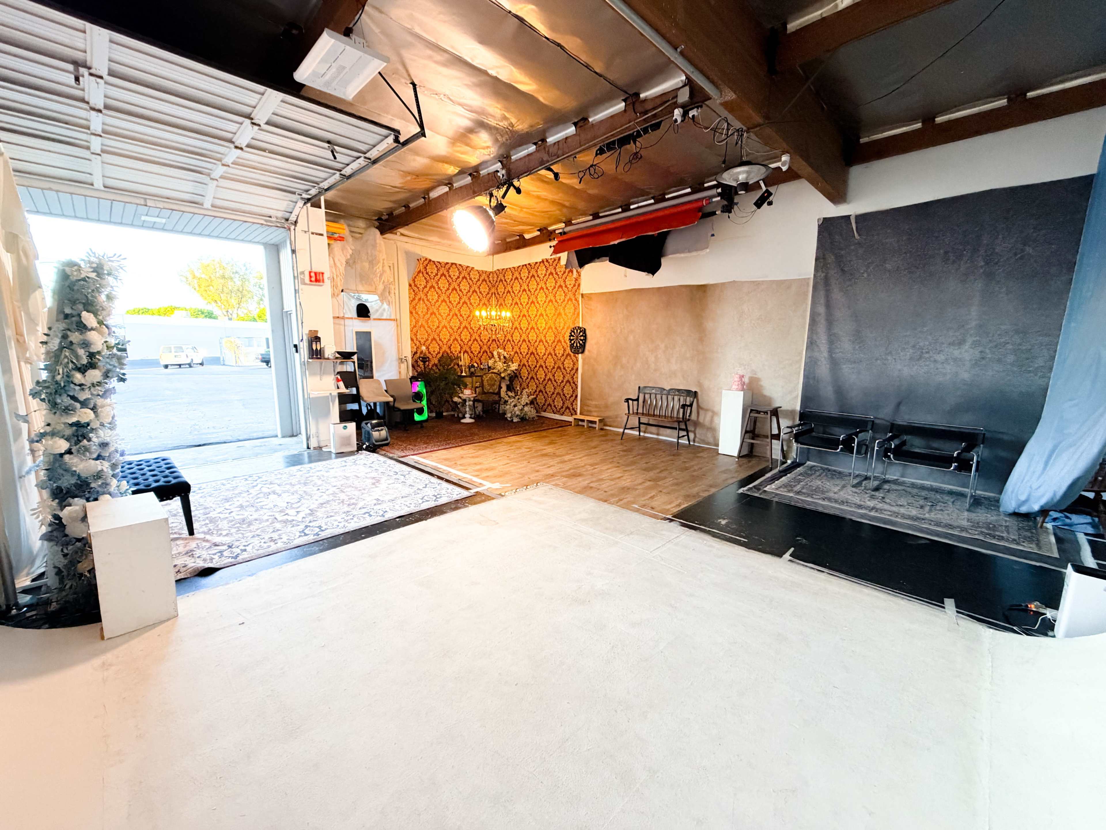 The image shows an indoor studio space featuring a mix of decorative elements, including a backdrop, seating areas, and lighting equipment.