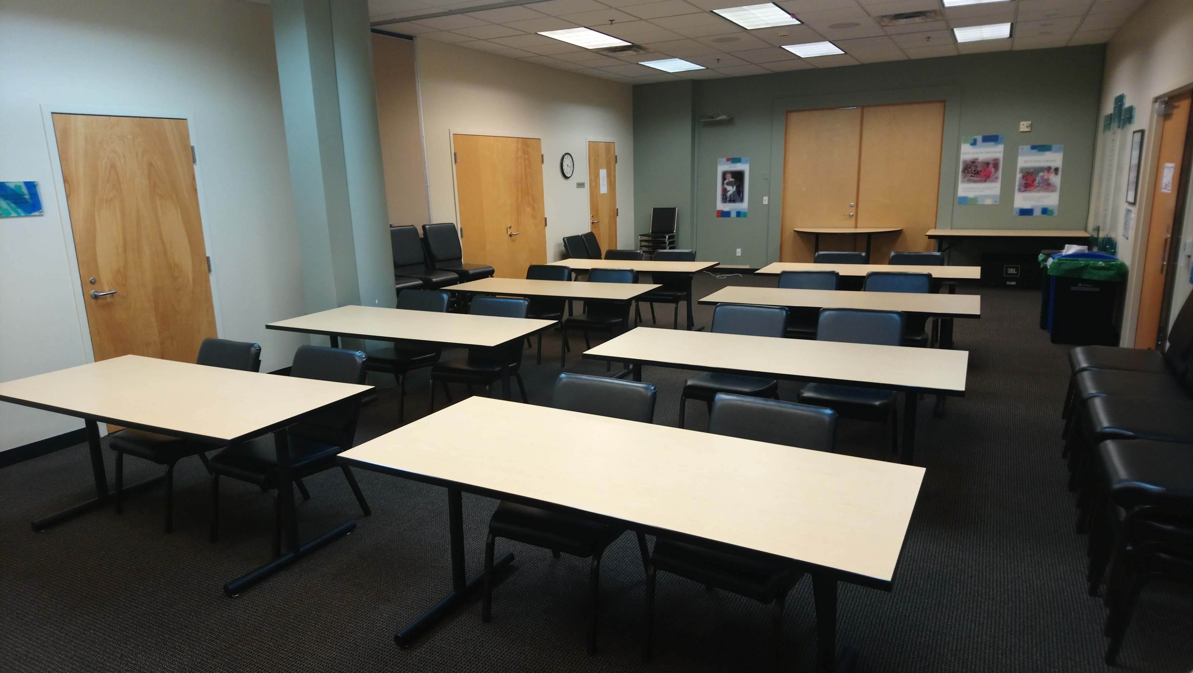 A meeting room with several tables and chairs arranged in a grid pattern, and two doors visible on one side.