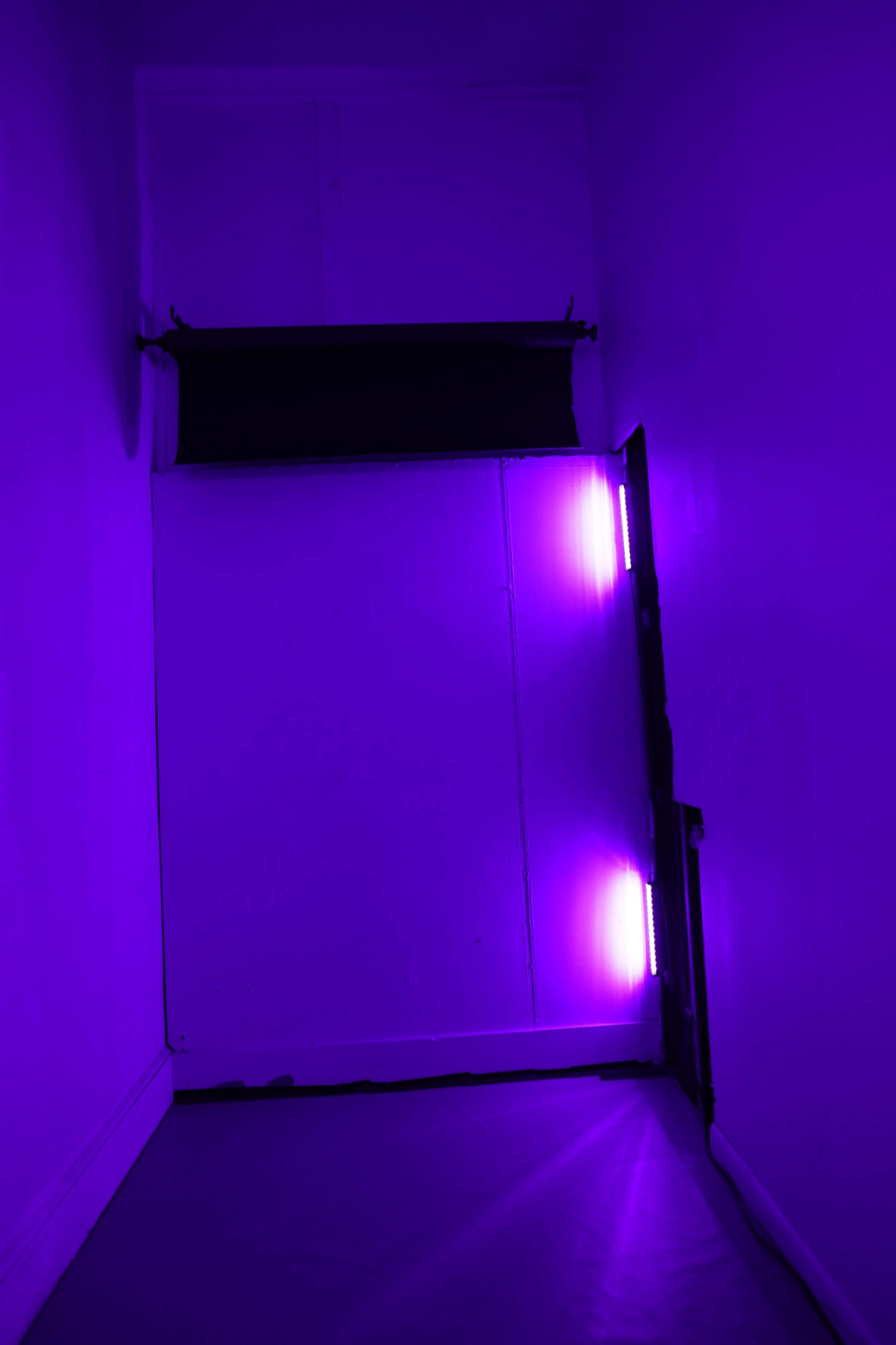 A dimly lit hallway features a large white door illuminated by purple lights on the right side.