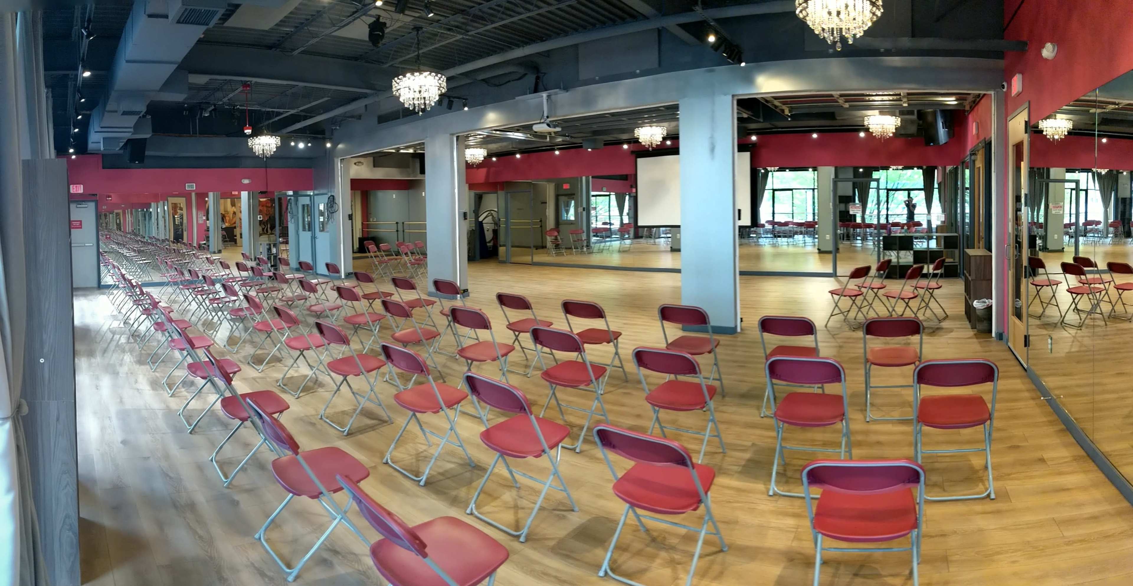 A spacious dance studio features several rows of red chairs aligned in front of large mirrors and windows.