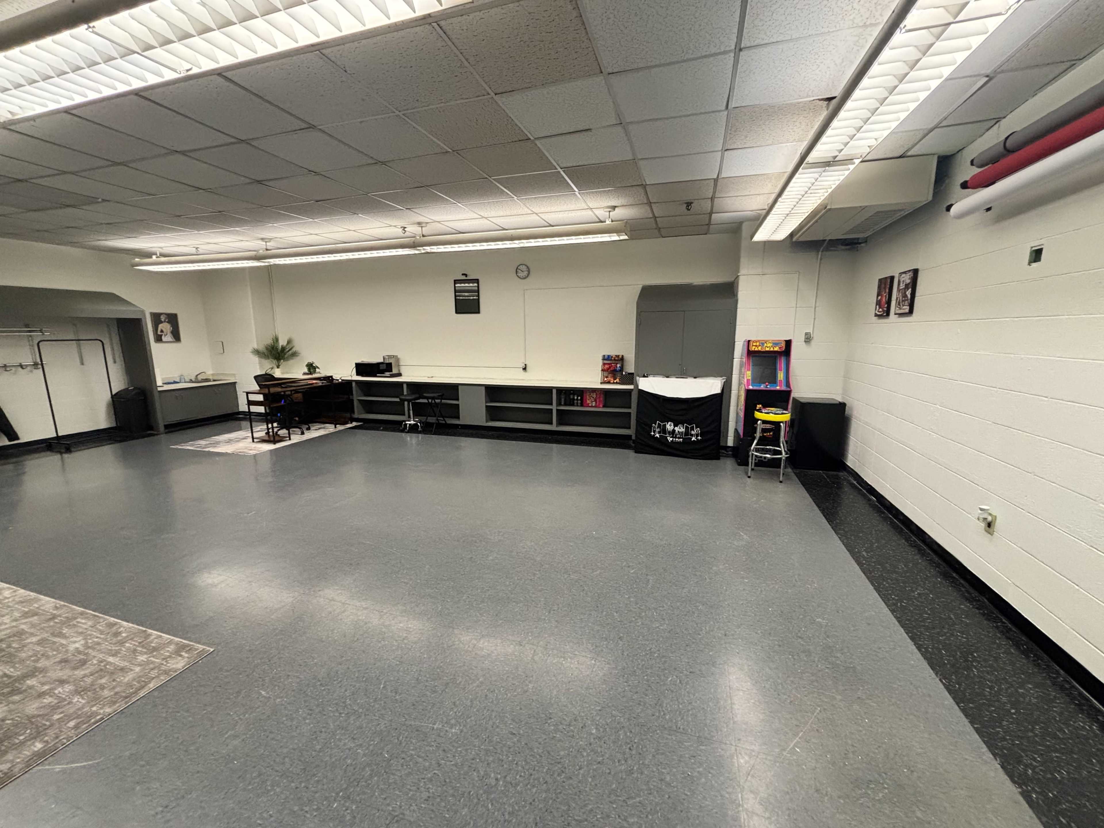 The image shows a spacious, empty室内 area with a gray floor, white walls, a counter along one side, and a small arcade machine on the right.