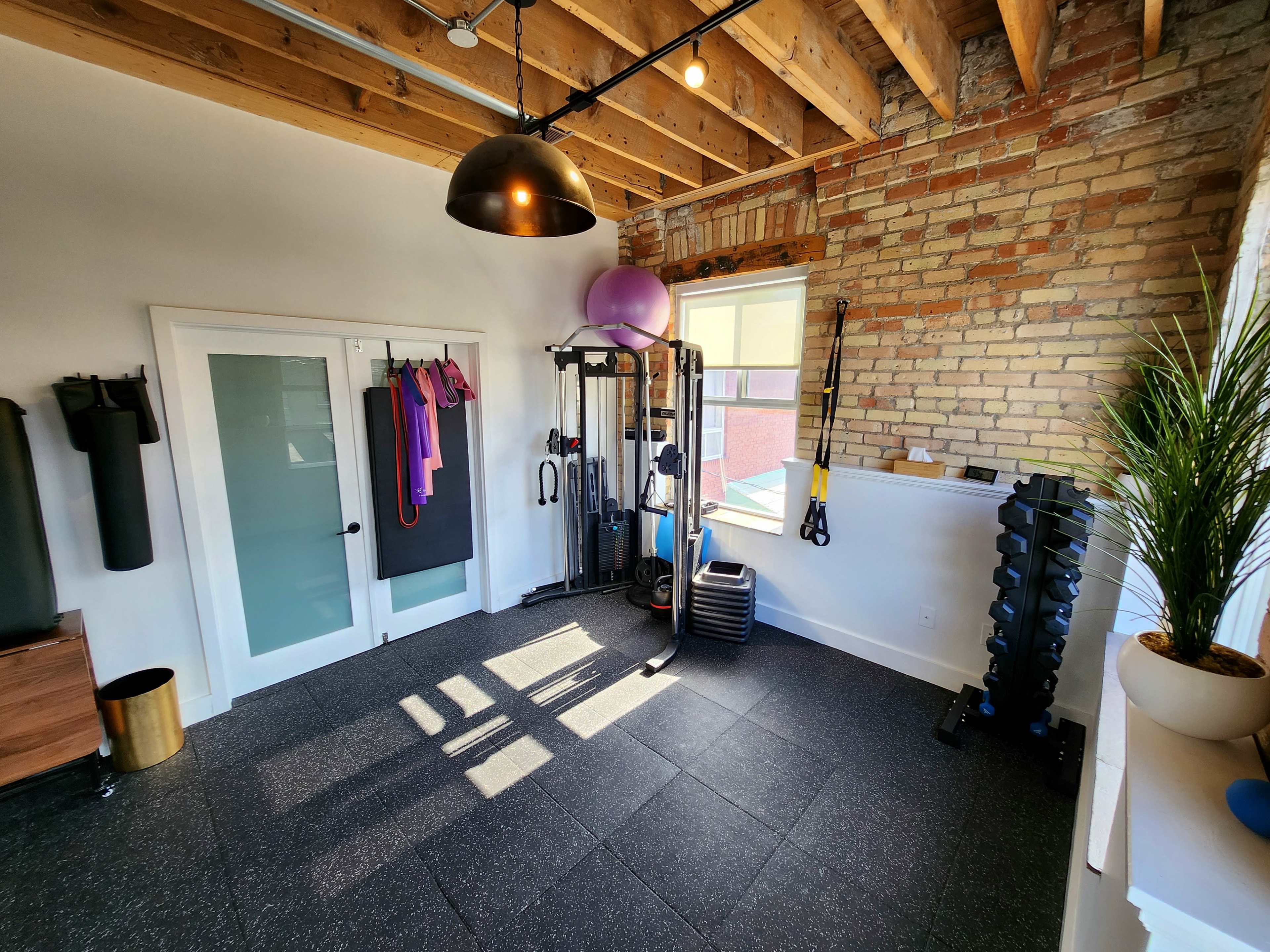 A well-equipped home gym featuring exercise equipment, weights, and fitness accessories in a room with exposed brick walls and wooden beams.