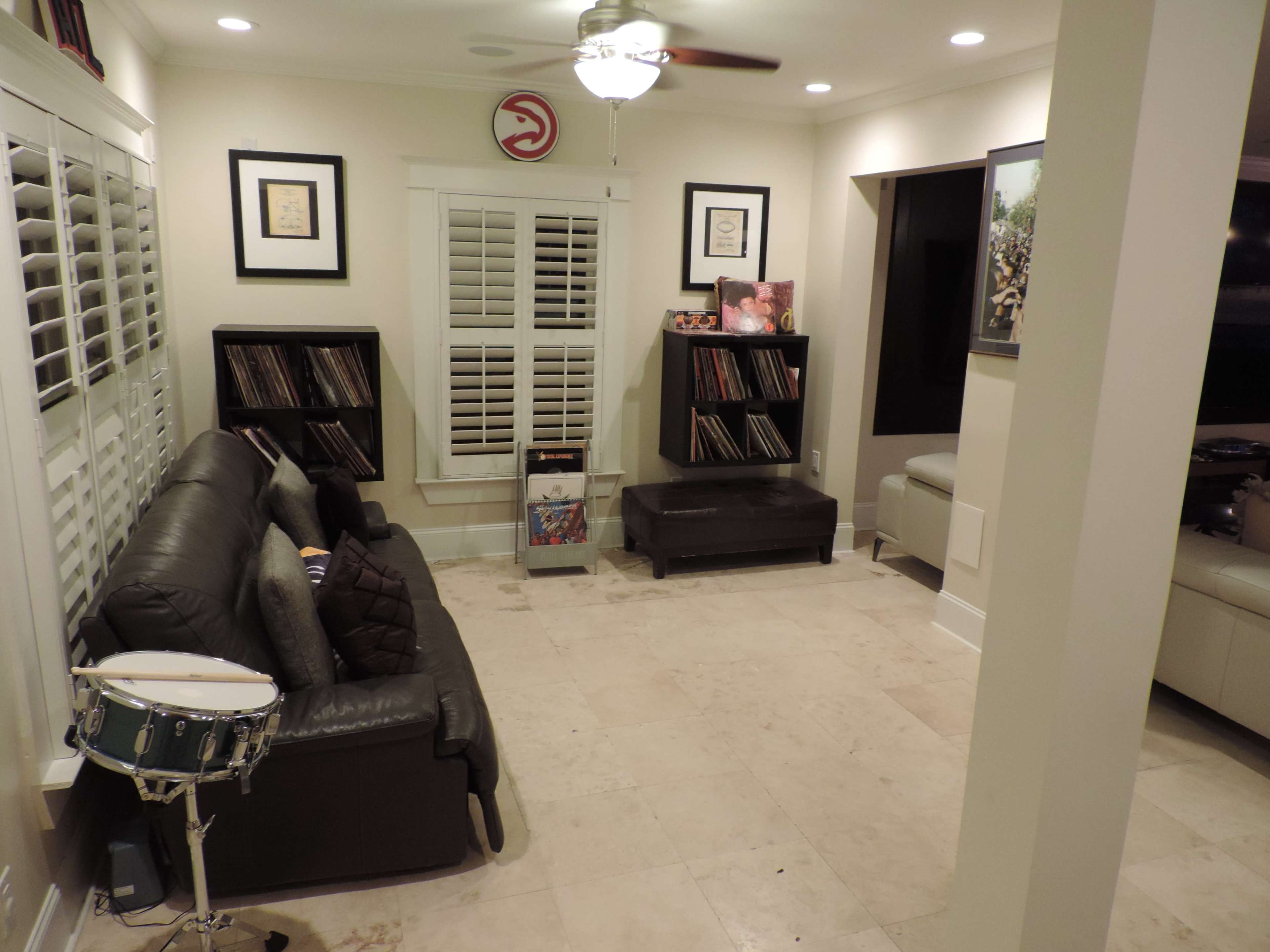 The image shows a living room with a sofa, a drum, and two shelves filled with records against the wall.