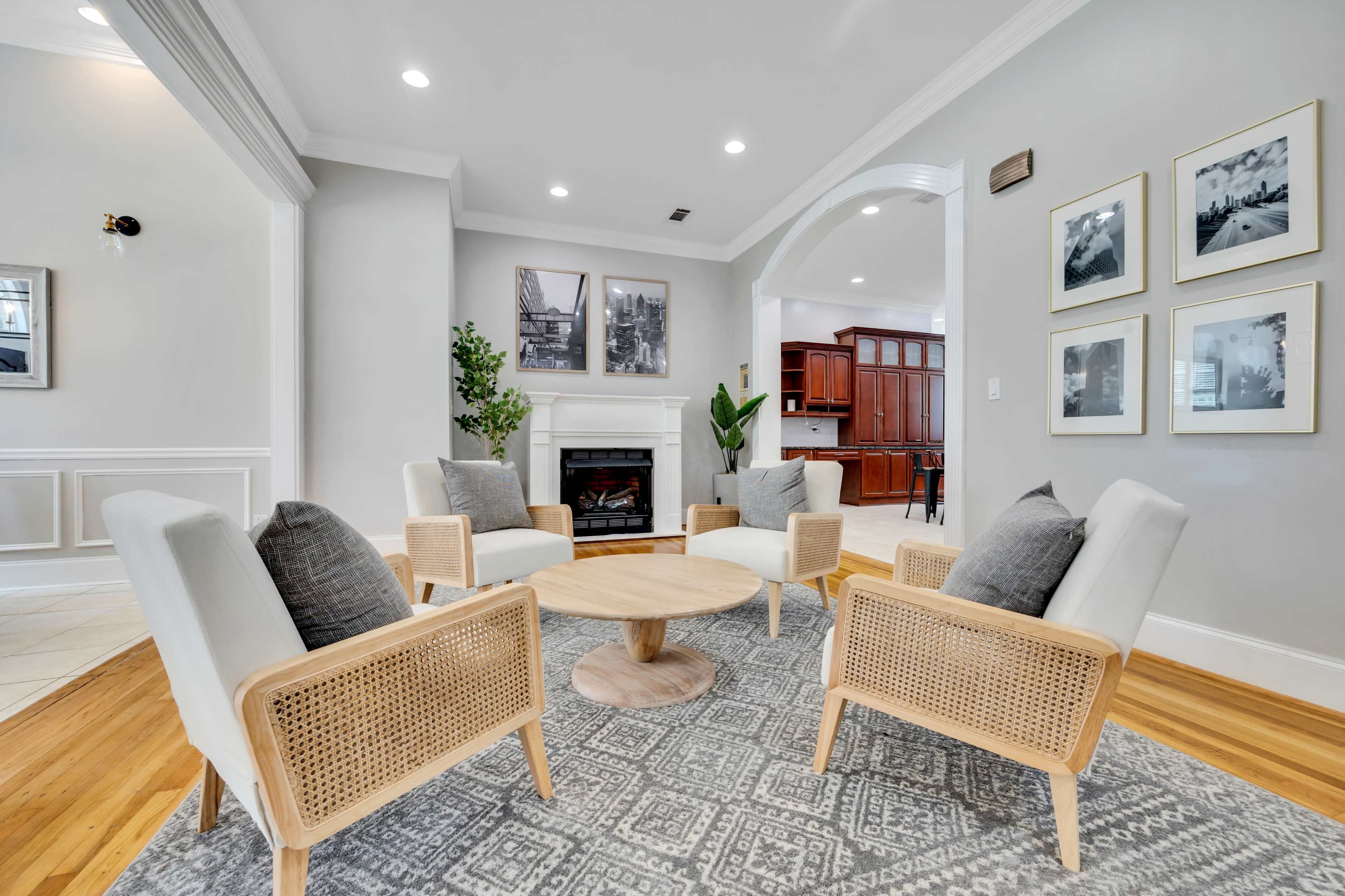 A modern living room features four armchairs arranged around a circular wooden table, with a fireplace in the background and framed photos on the walls.