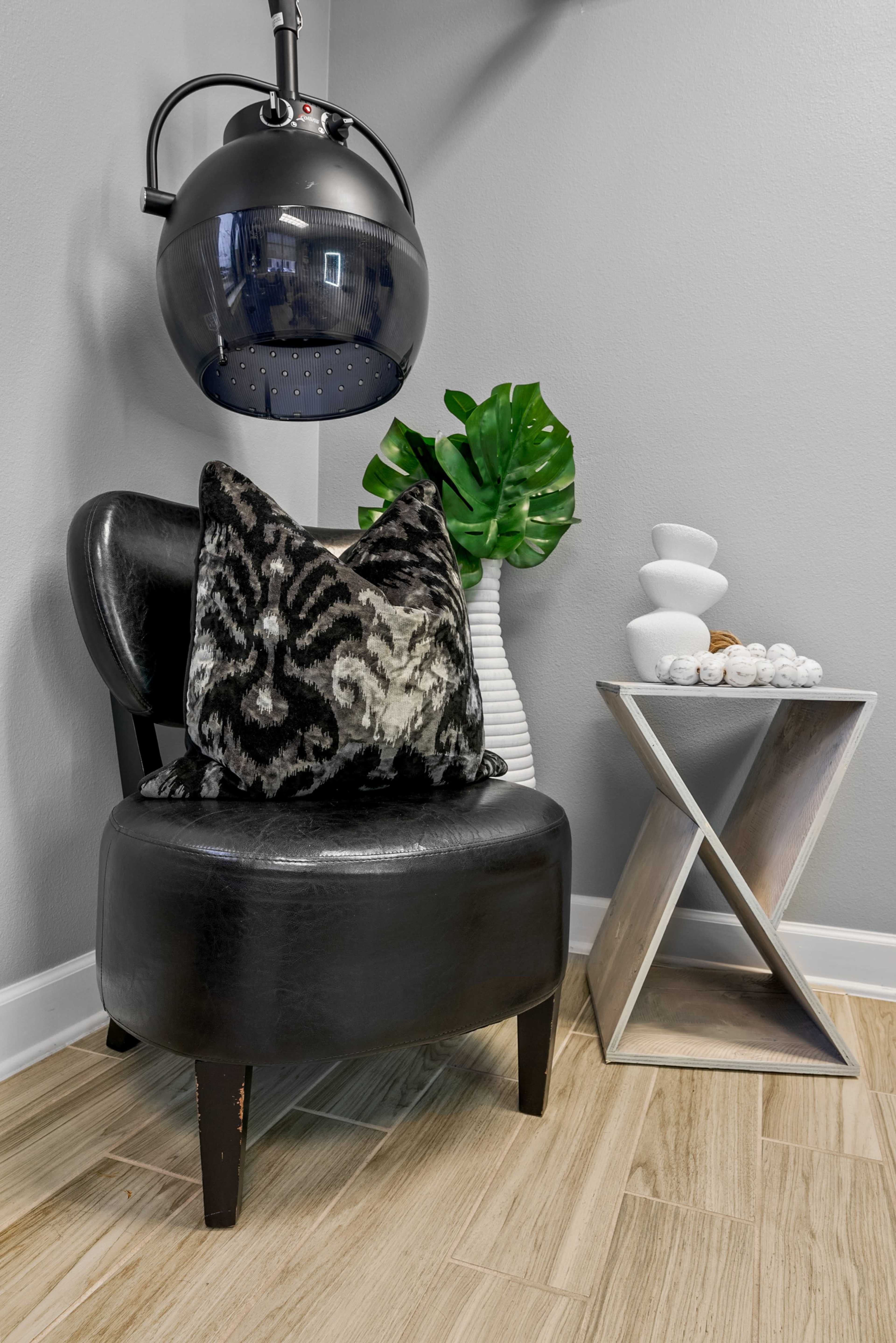 A black chair with a patterned pillow sits next to a decorative plant and a modern side table in a well-lit room.