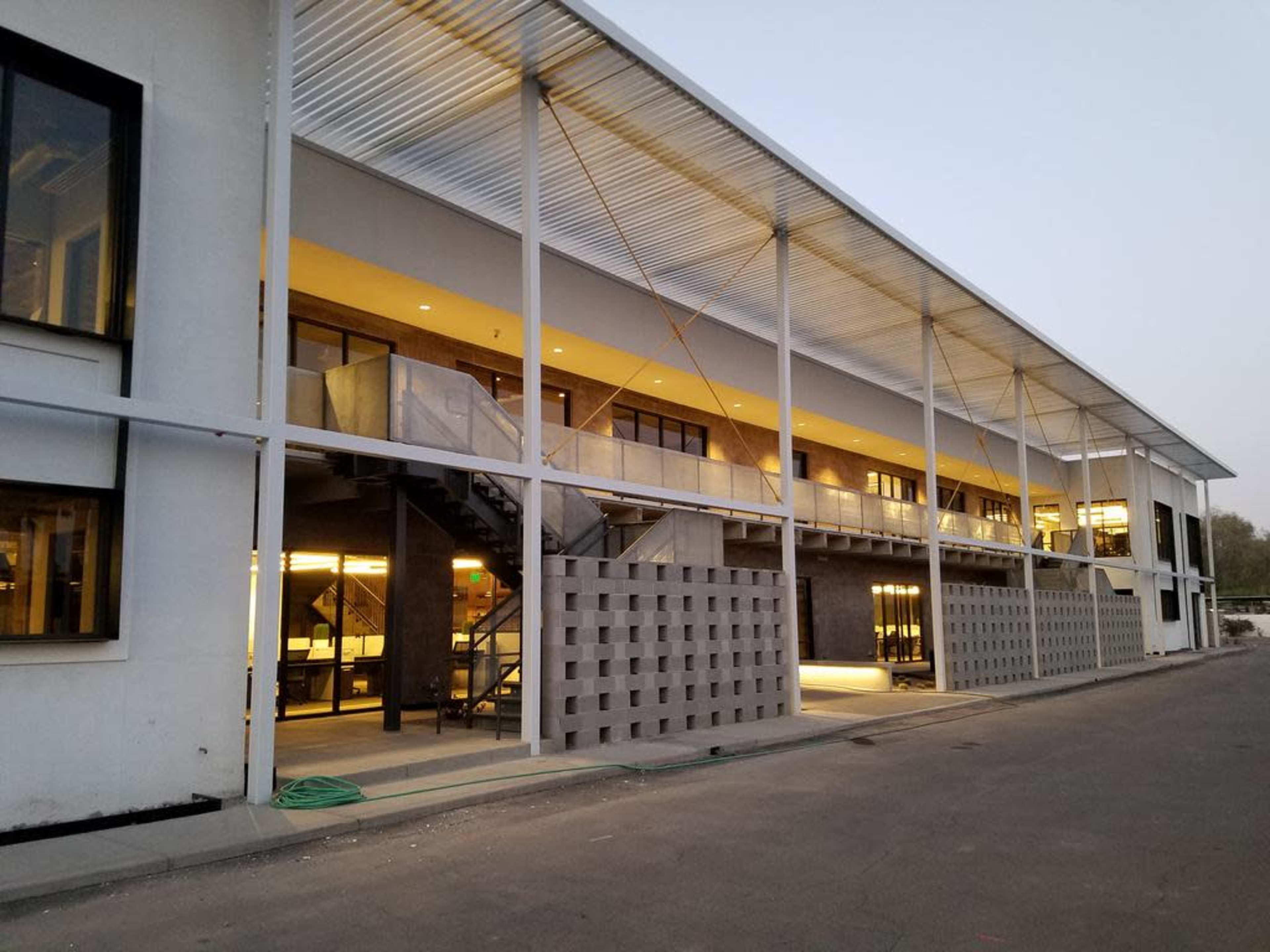 The image shows a modern building with a two-story structure, featuring large windows, a concrete facade, and an outdoor staircase.