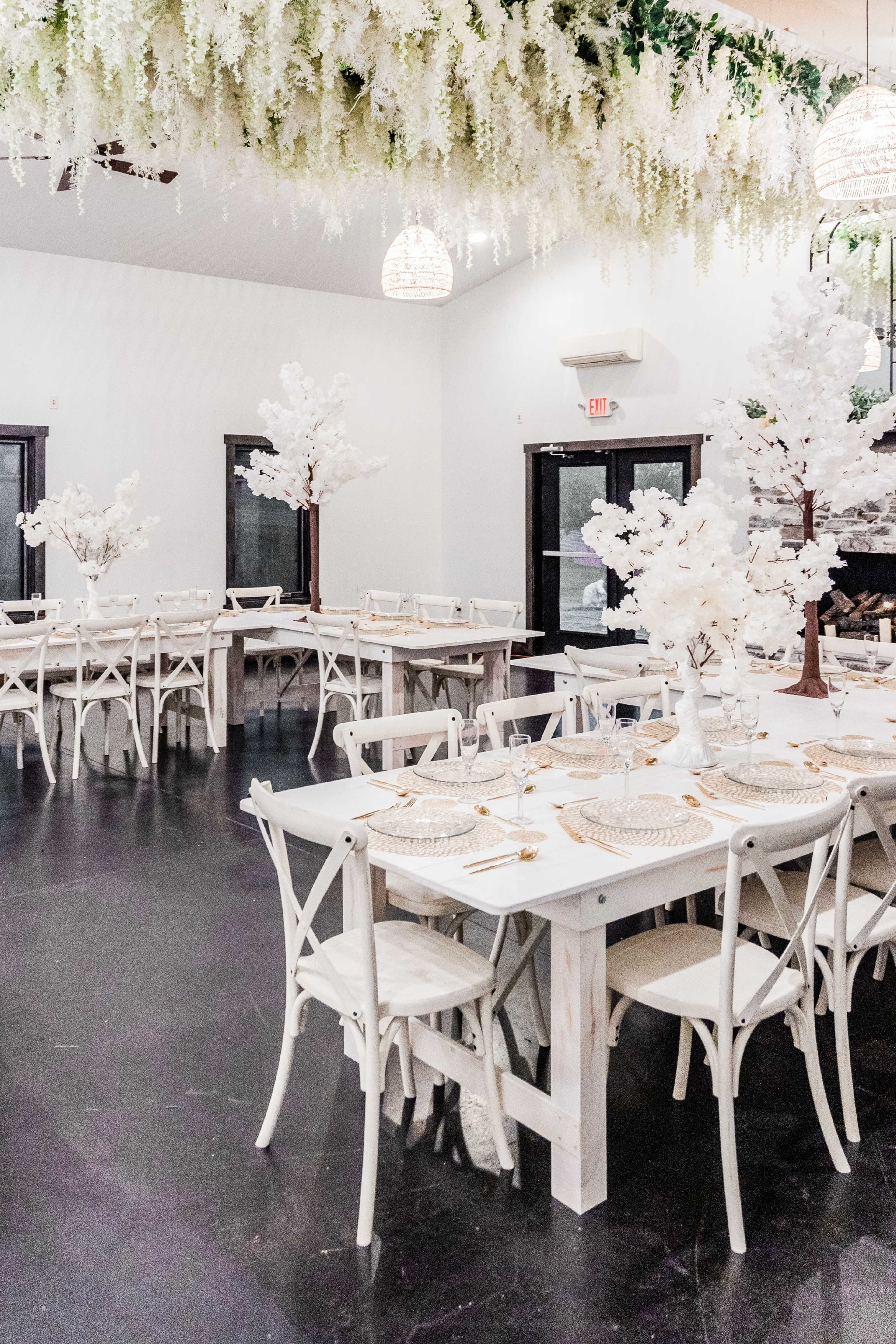 A spacious dining area set with white tables and chairs, adorned with floral decorations and pendant lights overhead.