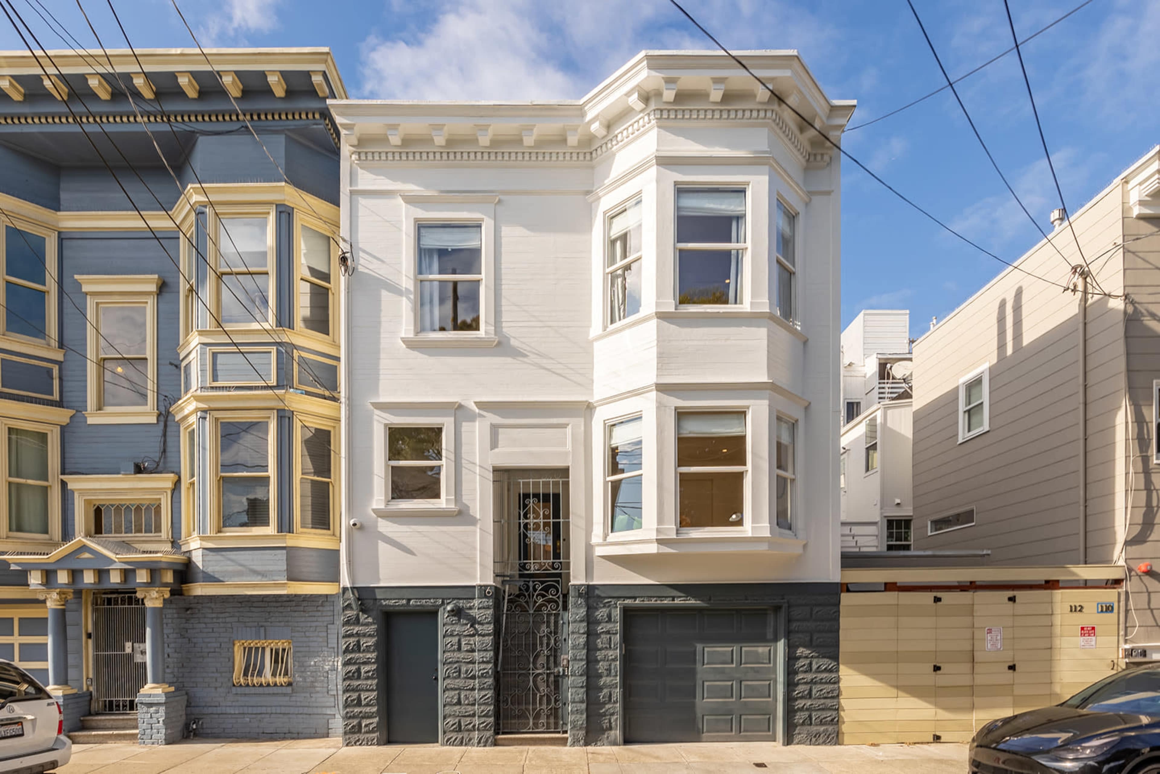 A two-story residential building with a bay window is flanked by two other homes, featuring distinct architectural styles and colors.