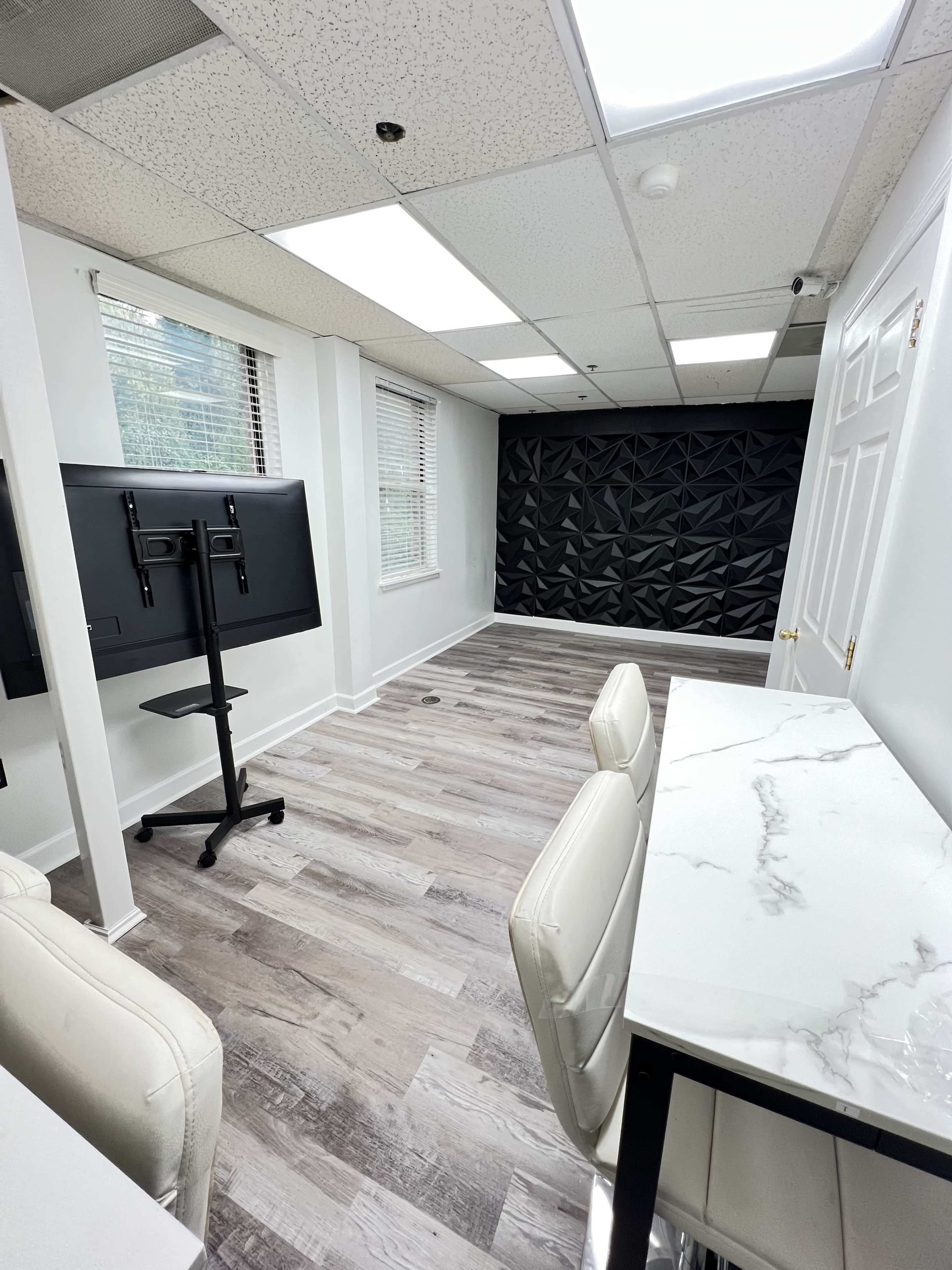 A modern office space featuring a black accent wall, a desk with white chairs, and a mounted television on a stand.