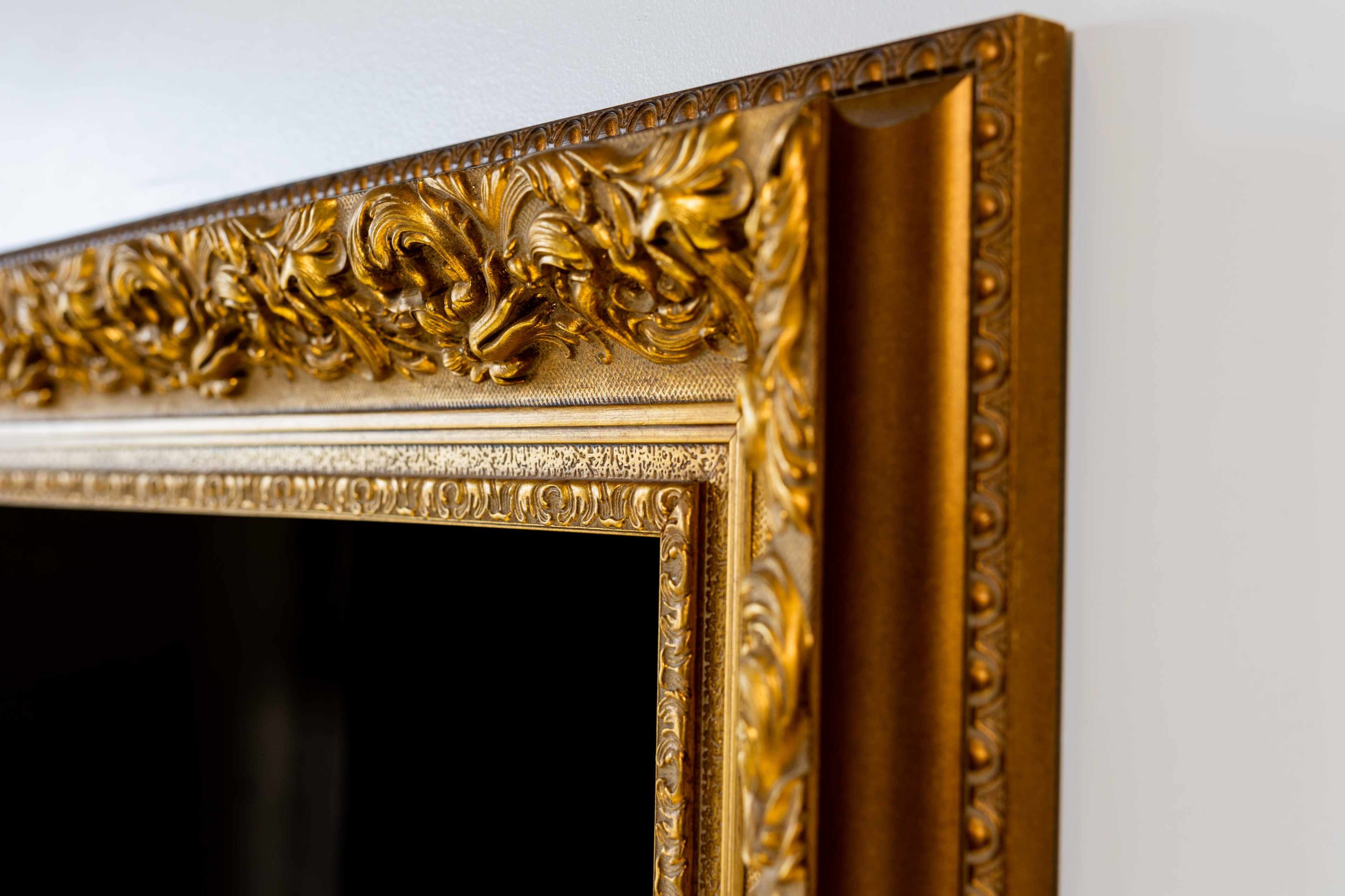 A close-up of a decorative, ornate gold picture frame against a white wall.
