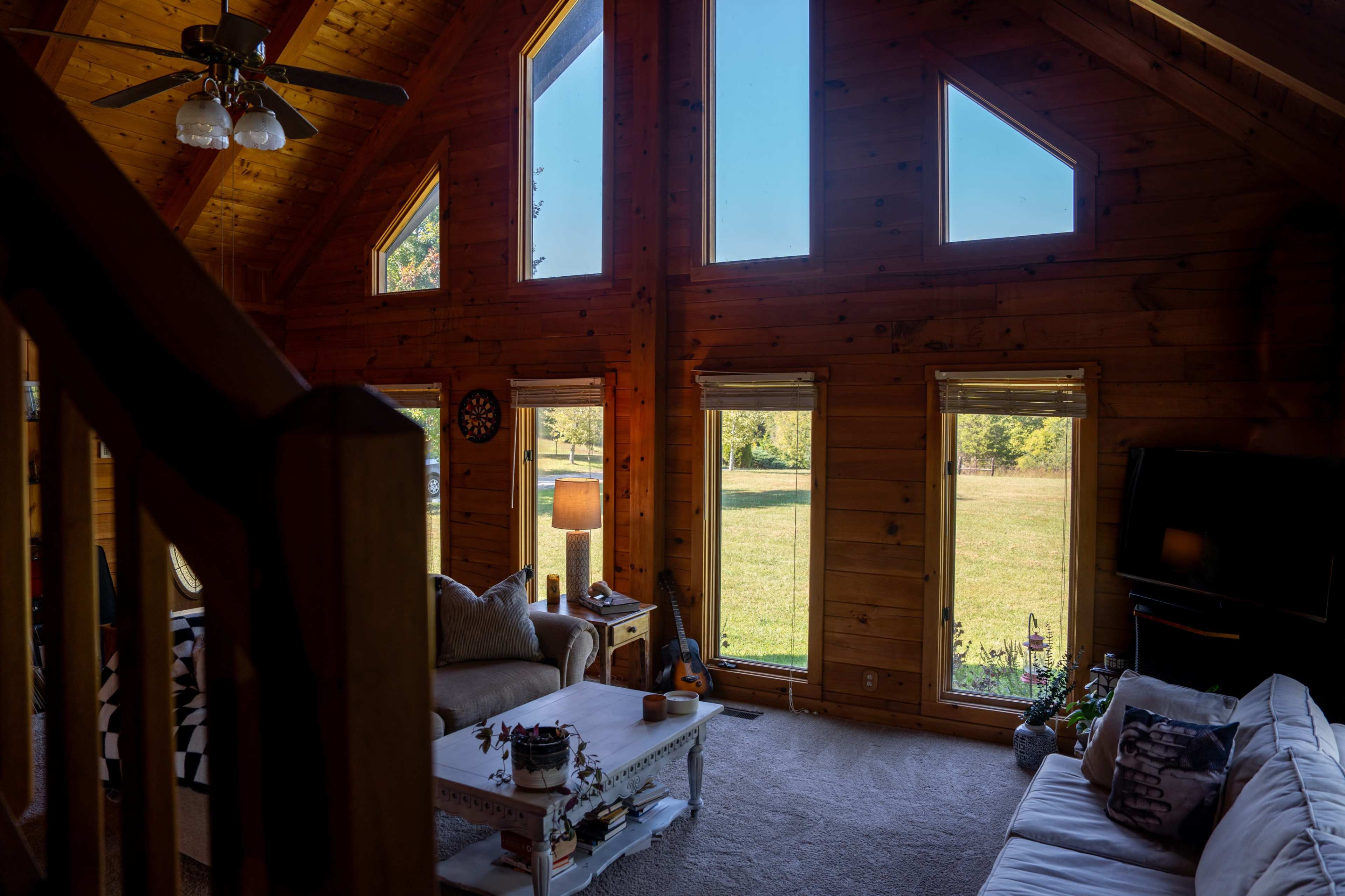 A spacious wooden living room with large windows that provide a view of the outdoors, featuring comfortable furniture and decorative elements.