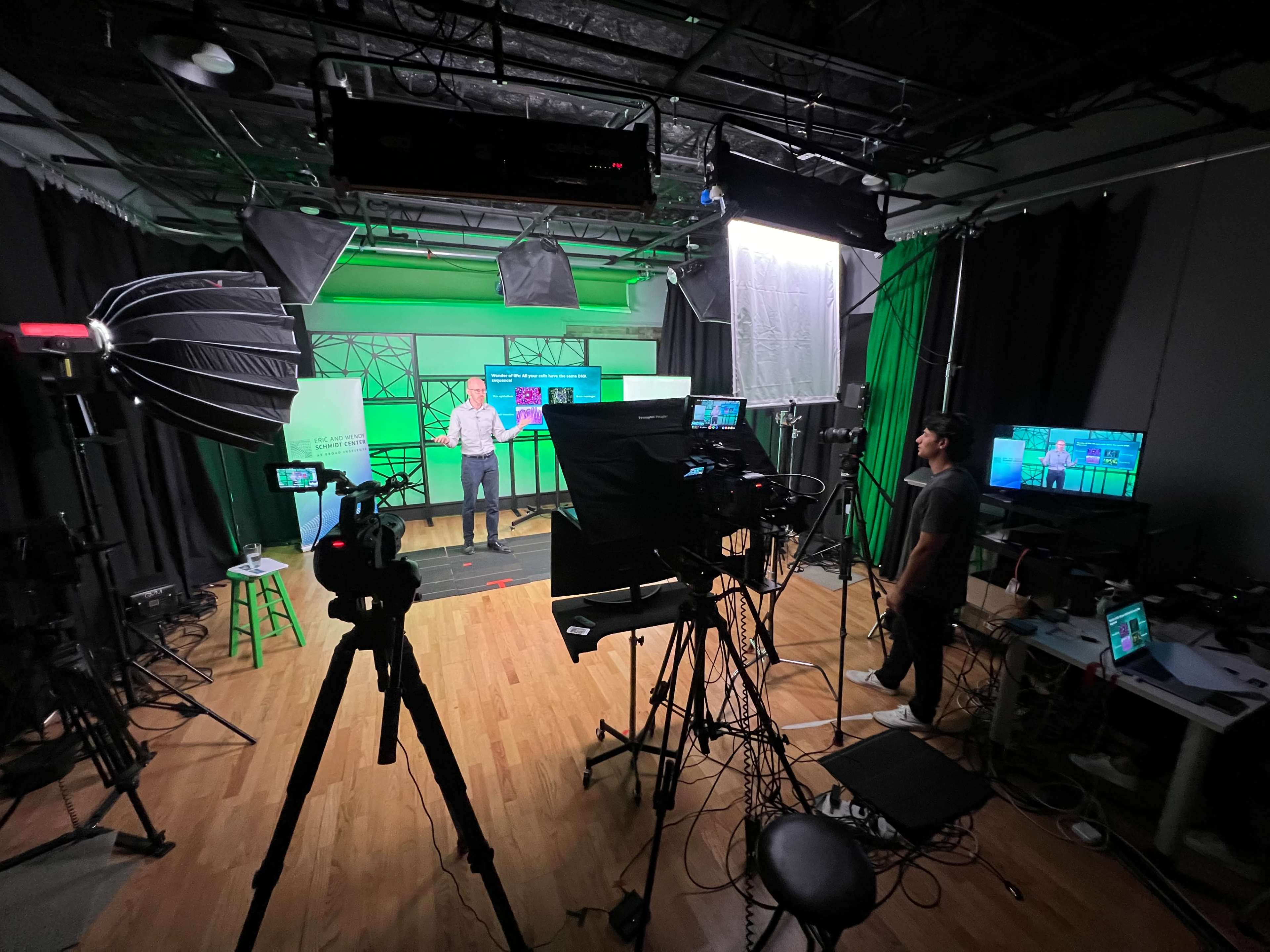 A person stands in a studio set up with multiple cameras and lighting equipment, preparing for a recording.