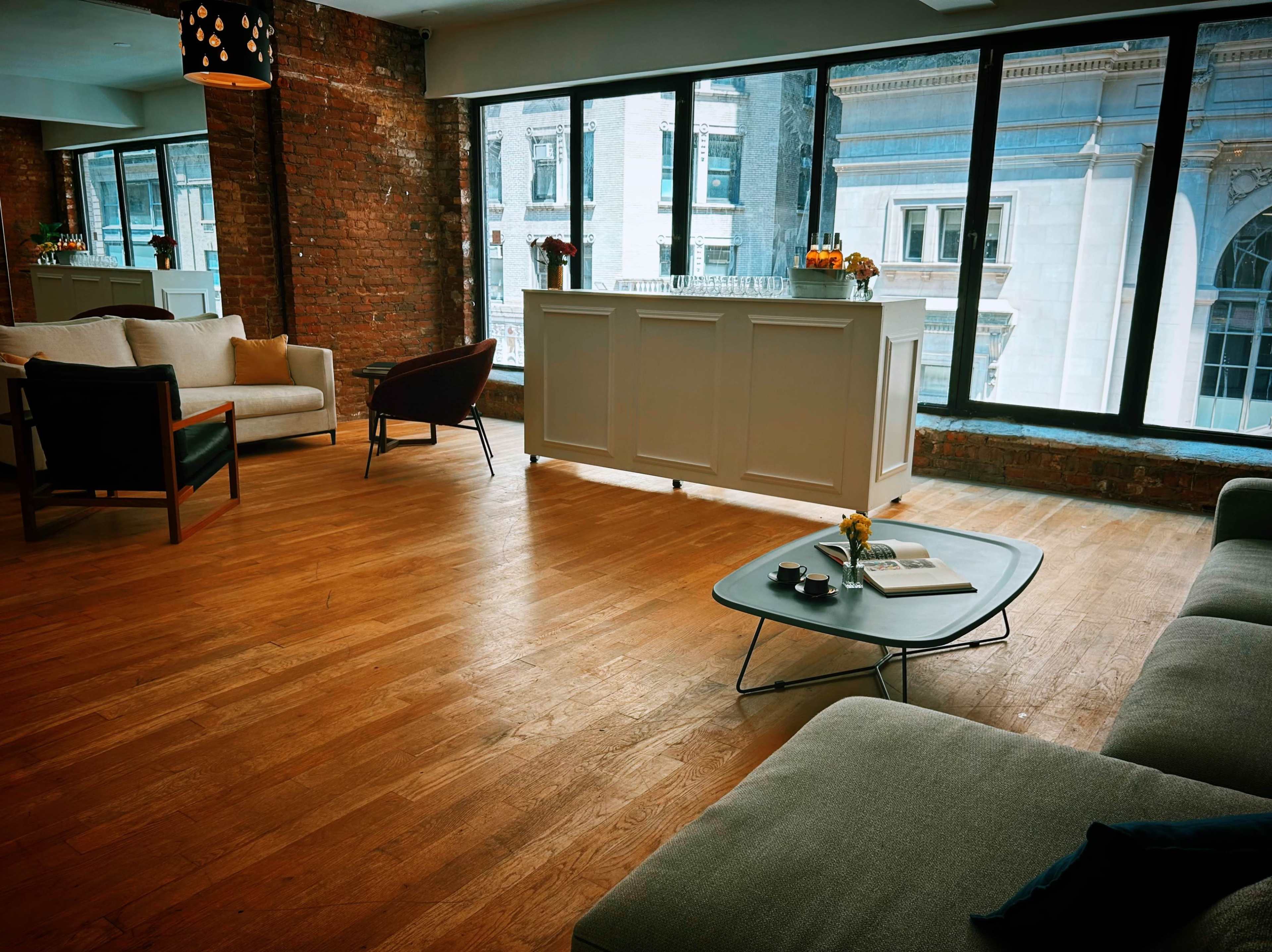 A modern, open space with large windows, wooden floors, and a white service counter in the background.