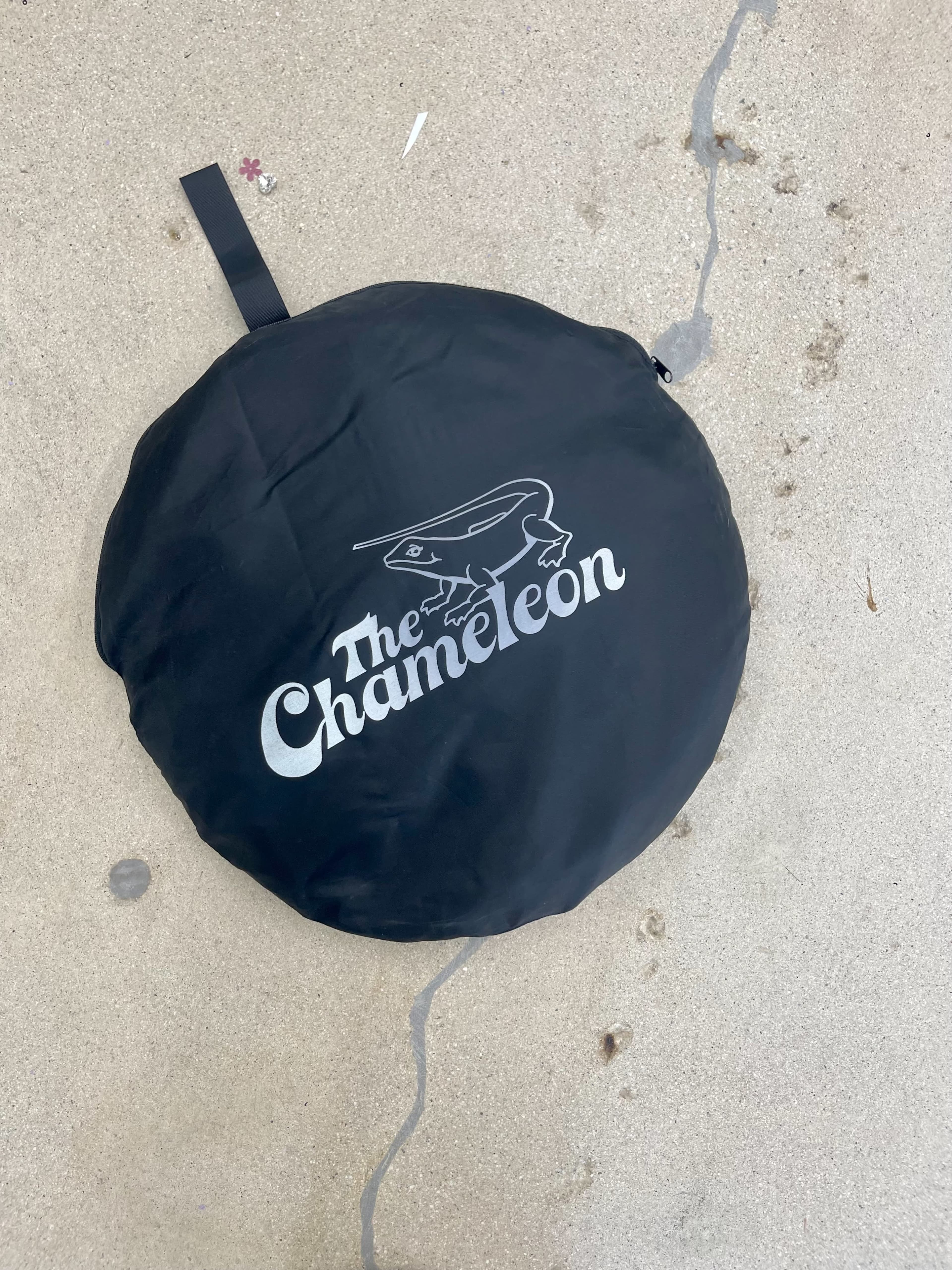 A black circular bag labeled "The Chameleon" is resting on a concrete surface.