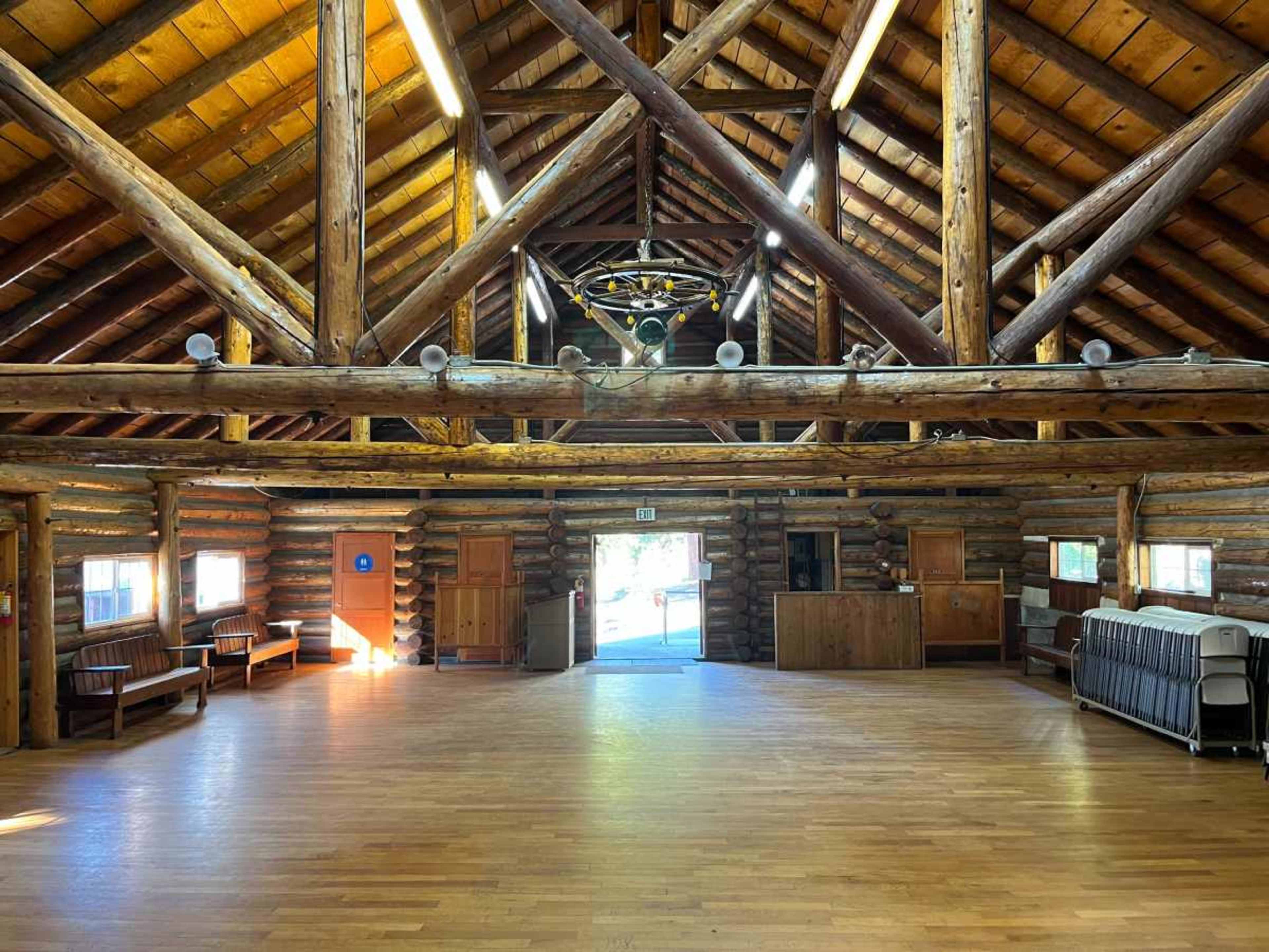 The image shows a spacious lodge interior with log walls, wooden beams, and several benches along the sides.