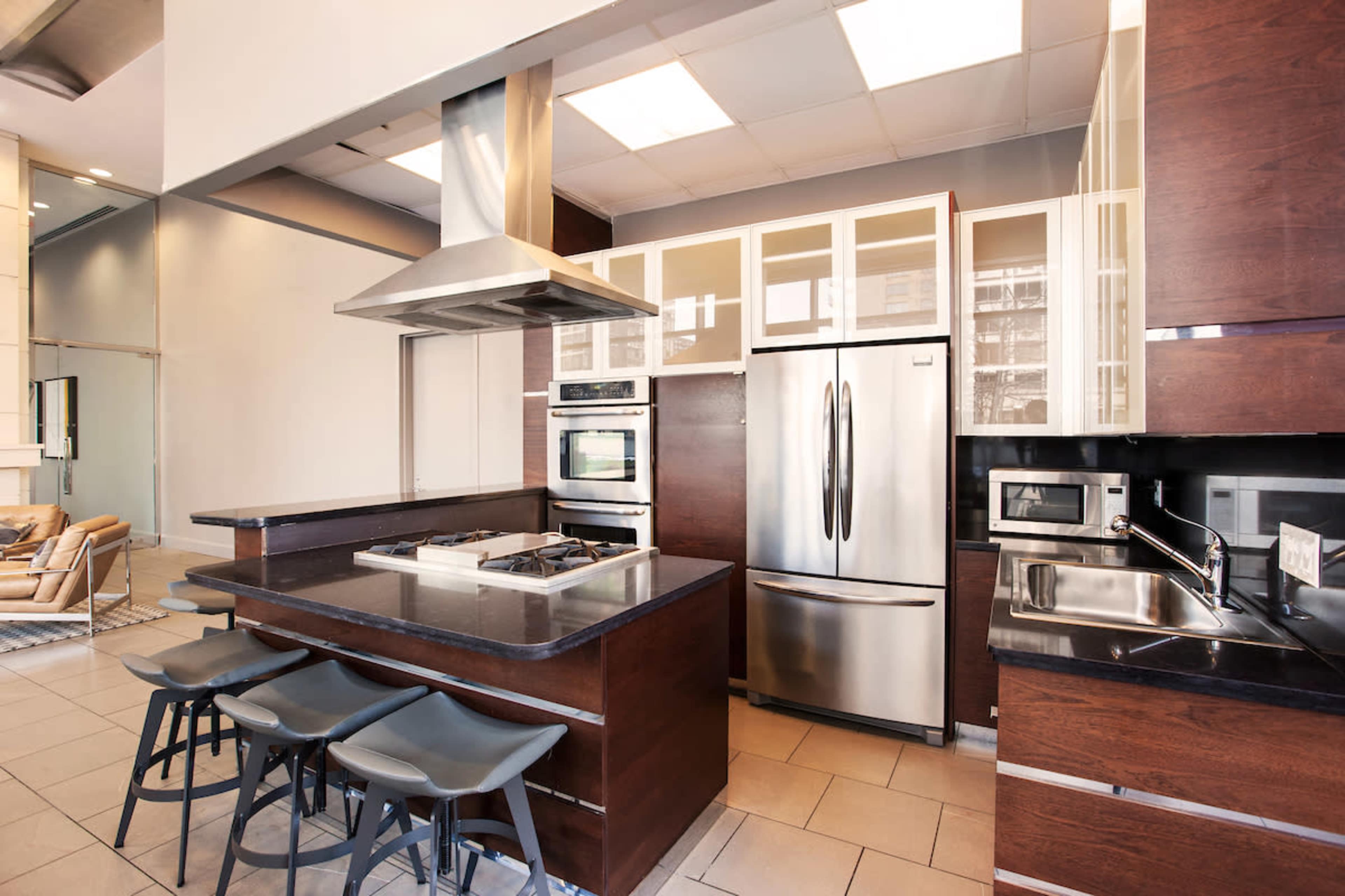 The image shows a modern kitchen featuring stainless steel appliances, a central island with seating, and cabinetry with glass doors.