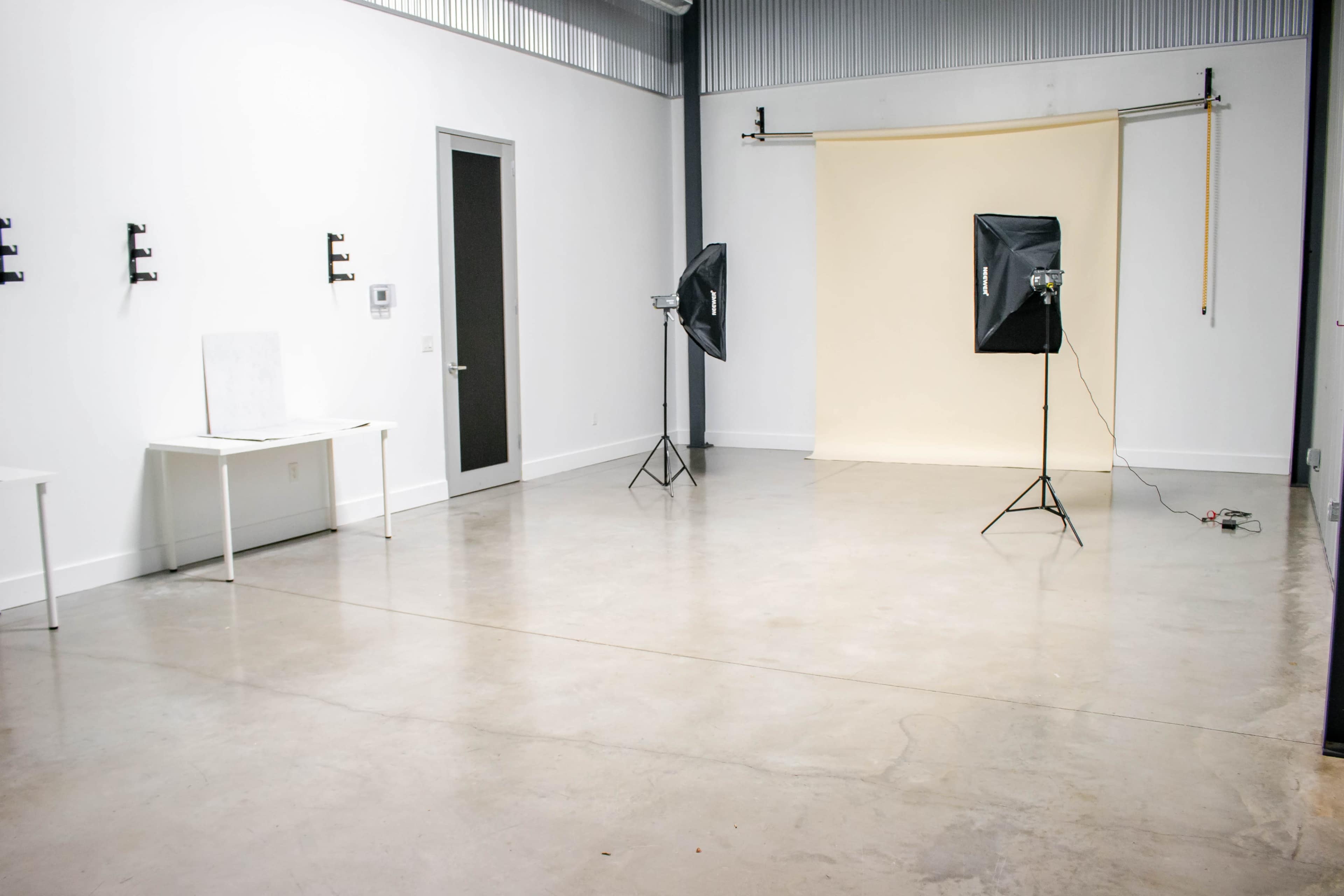 The scene shows a spacious, empty studio with a light-colored backdrop, two softbox lights, and a white table against a wall.