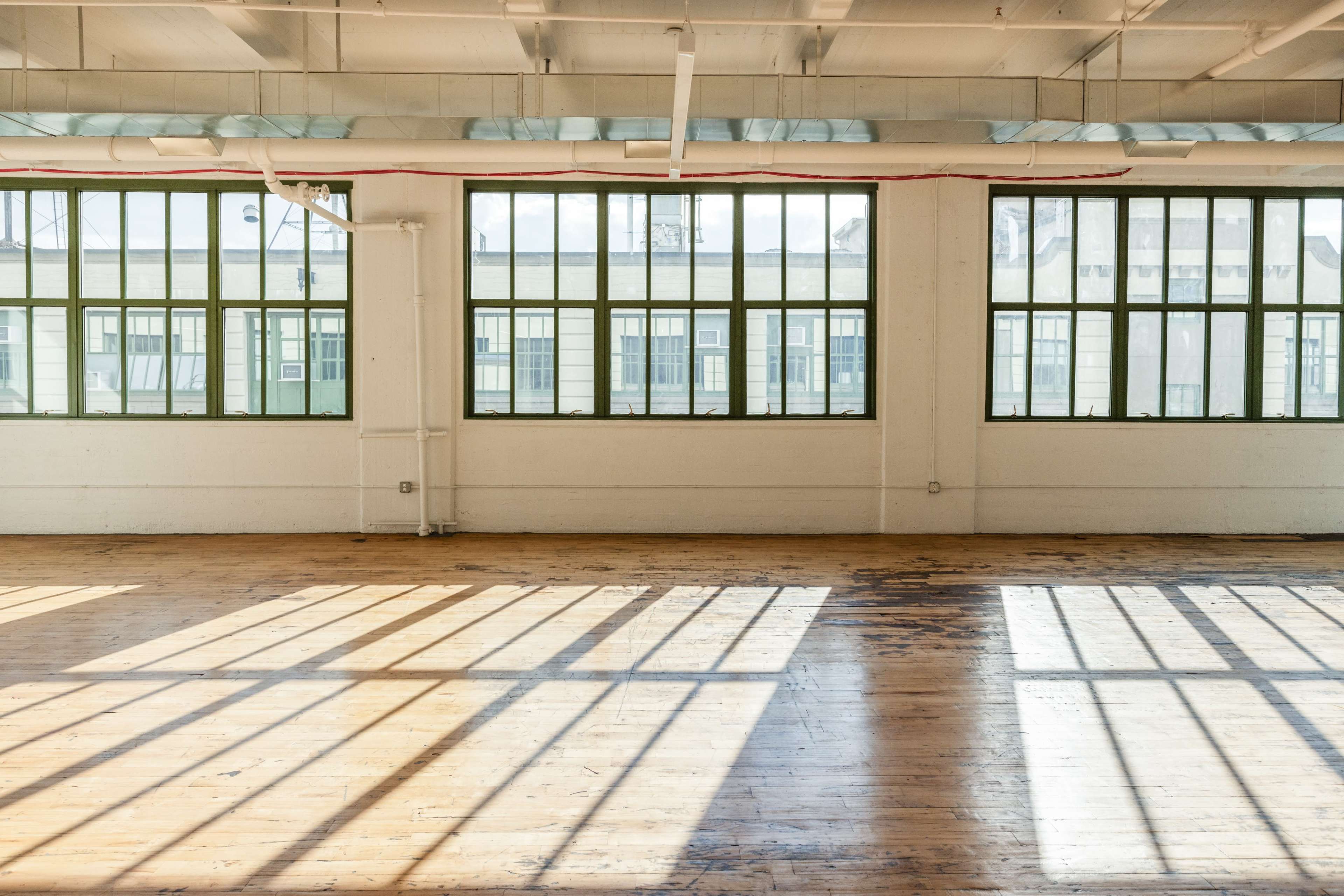 The image shows a spacious, well-lit room with large windows casting shadows on a wooden floor.