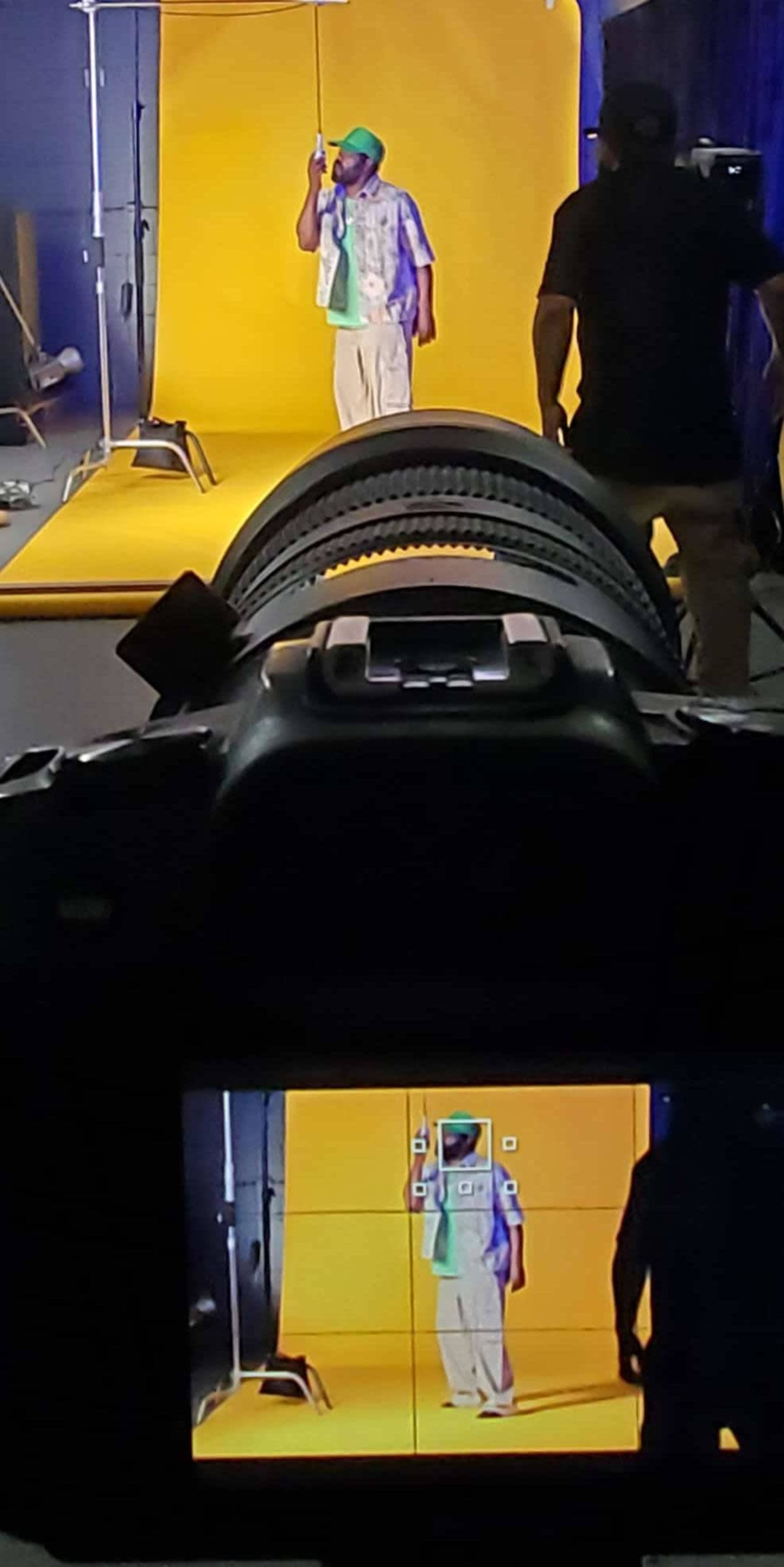 A photographer captures a subject in front of a bright yellow backdrop while another person adjusts the lighting equipment.