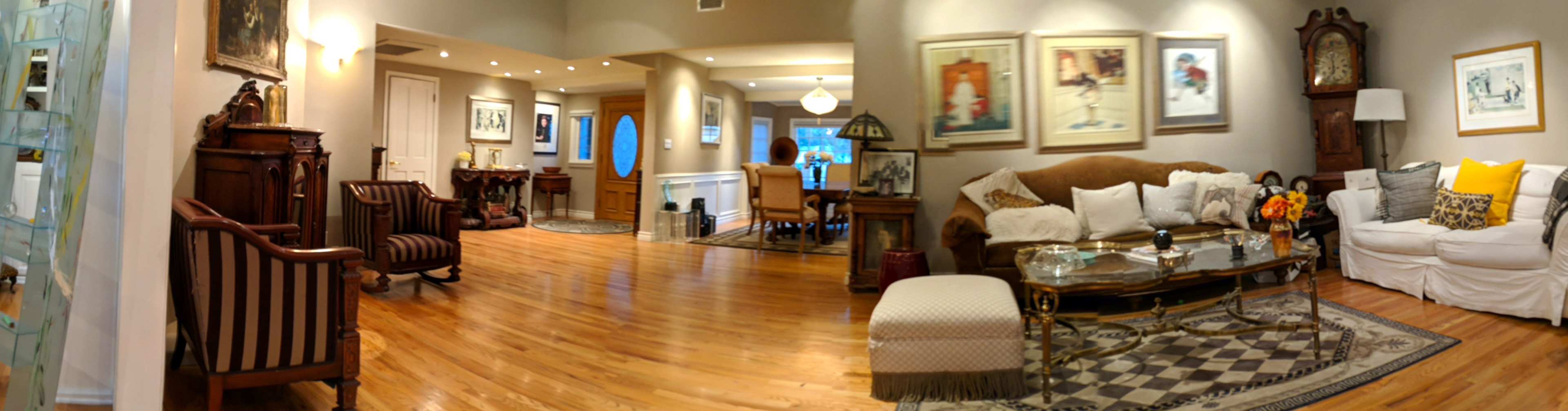 A spacious living area with wooden floors, a seating arrangement, wall art, and a dining area visible in the background.