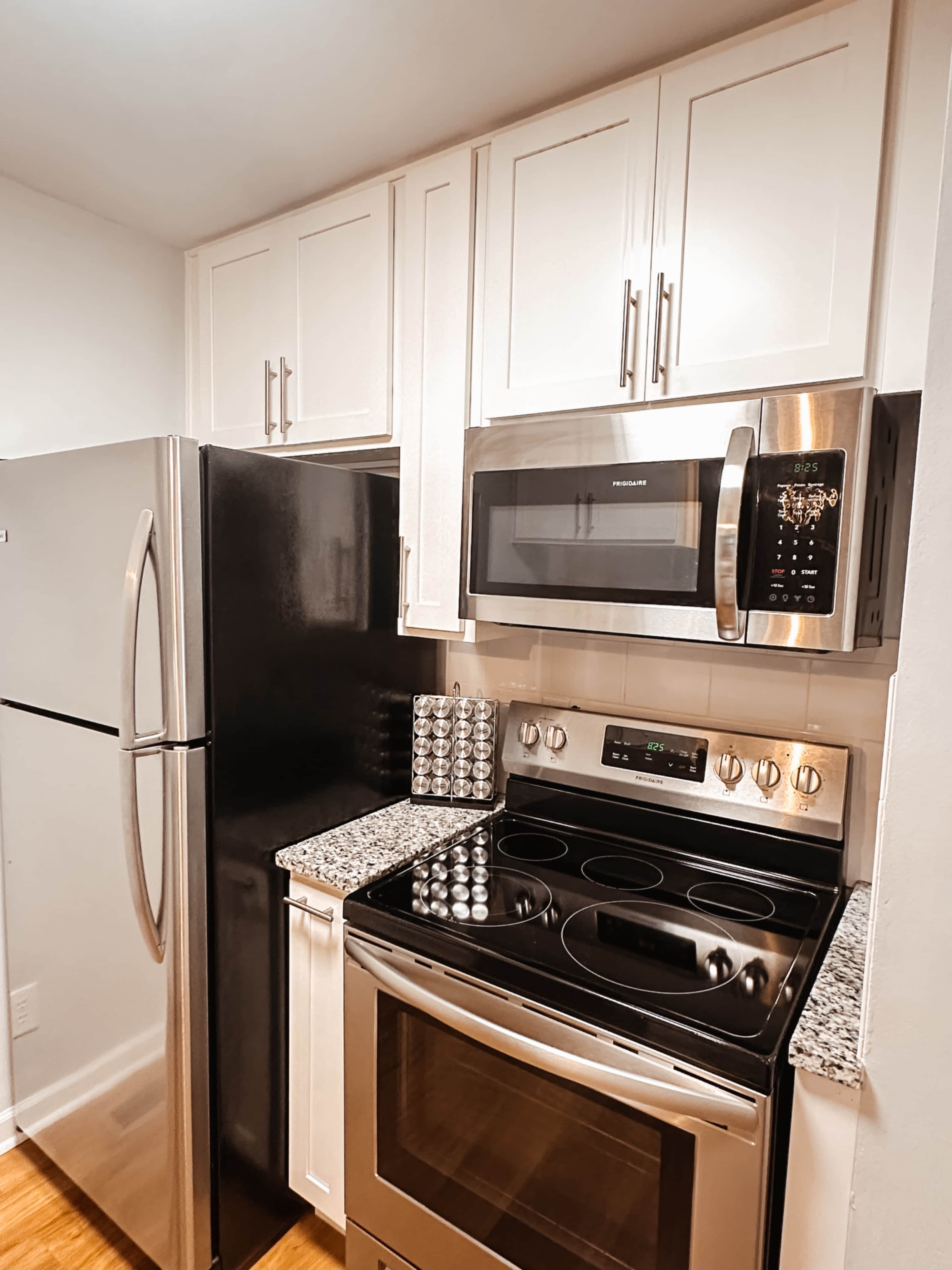 The image shows a modern kitchen with stainless steel appliances, including a refrigerator, microwave, and oven, set against white cabinets and a granite countertop.