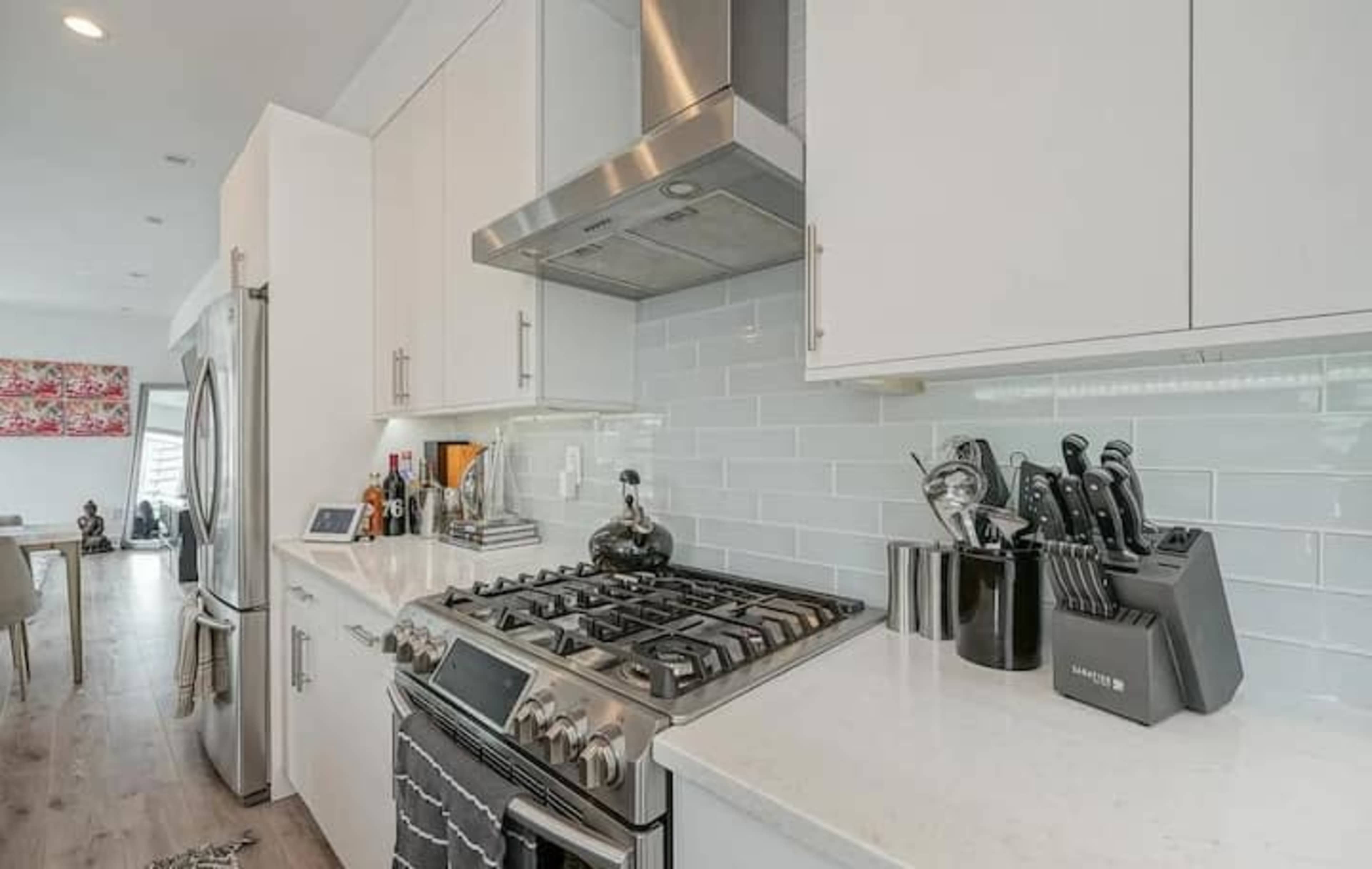 A modern kitchen with stainless steel appliances, white cabinetry, and a gas stove topped by a range hood.