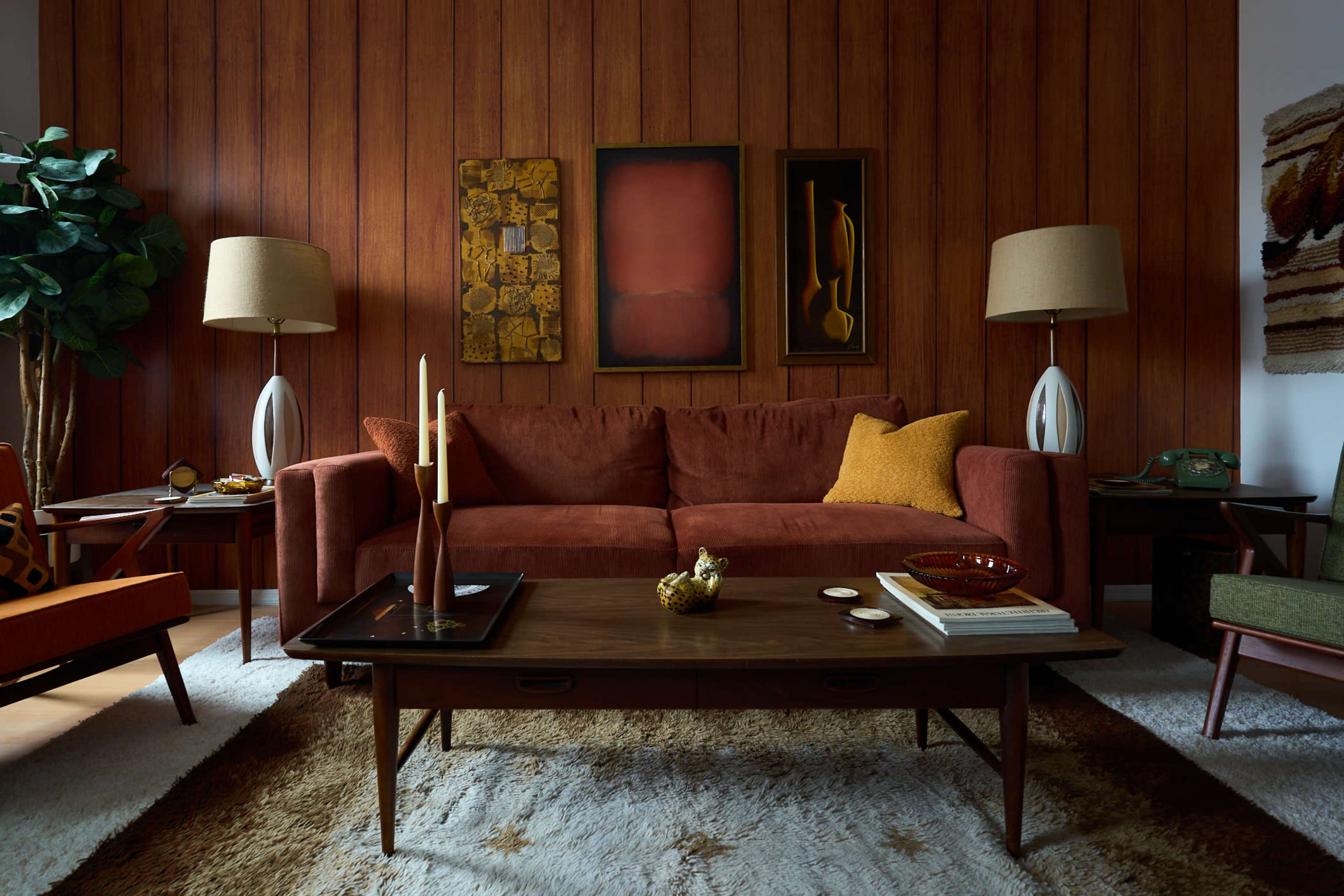 The image shows a cozy living room featuring a brown sofa, patterned wall art, and mid-century modern furniture, with a soft rug under a wooden coffee table.
