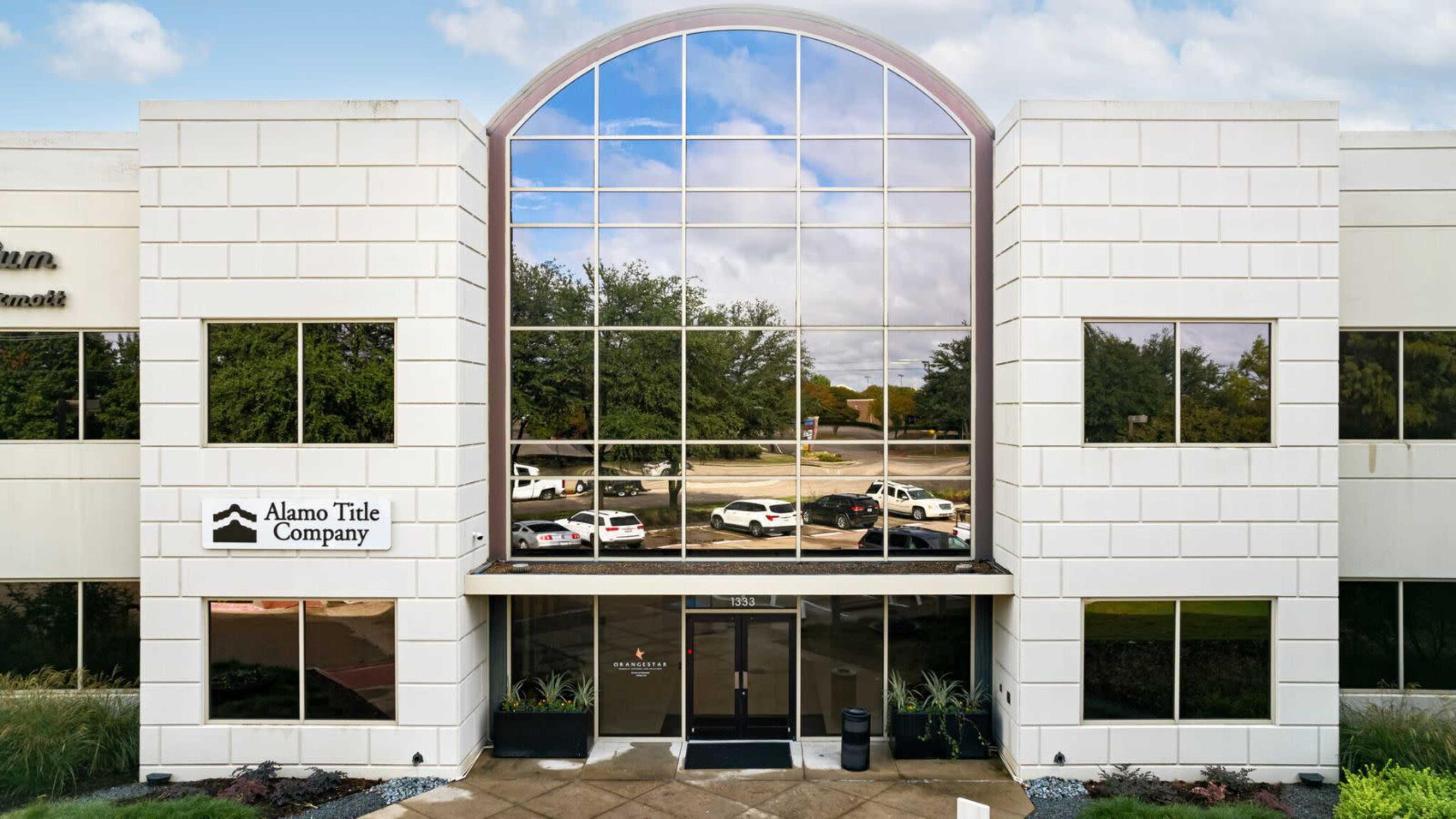 The image shows the entrance of a modern office building labeled "Alamo Title Company," featuring large glass windows and surrounding landscaping.