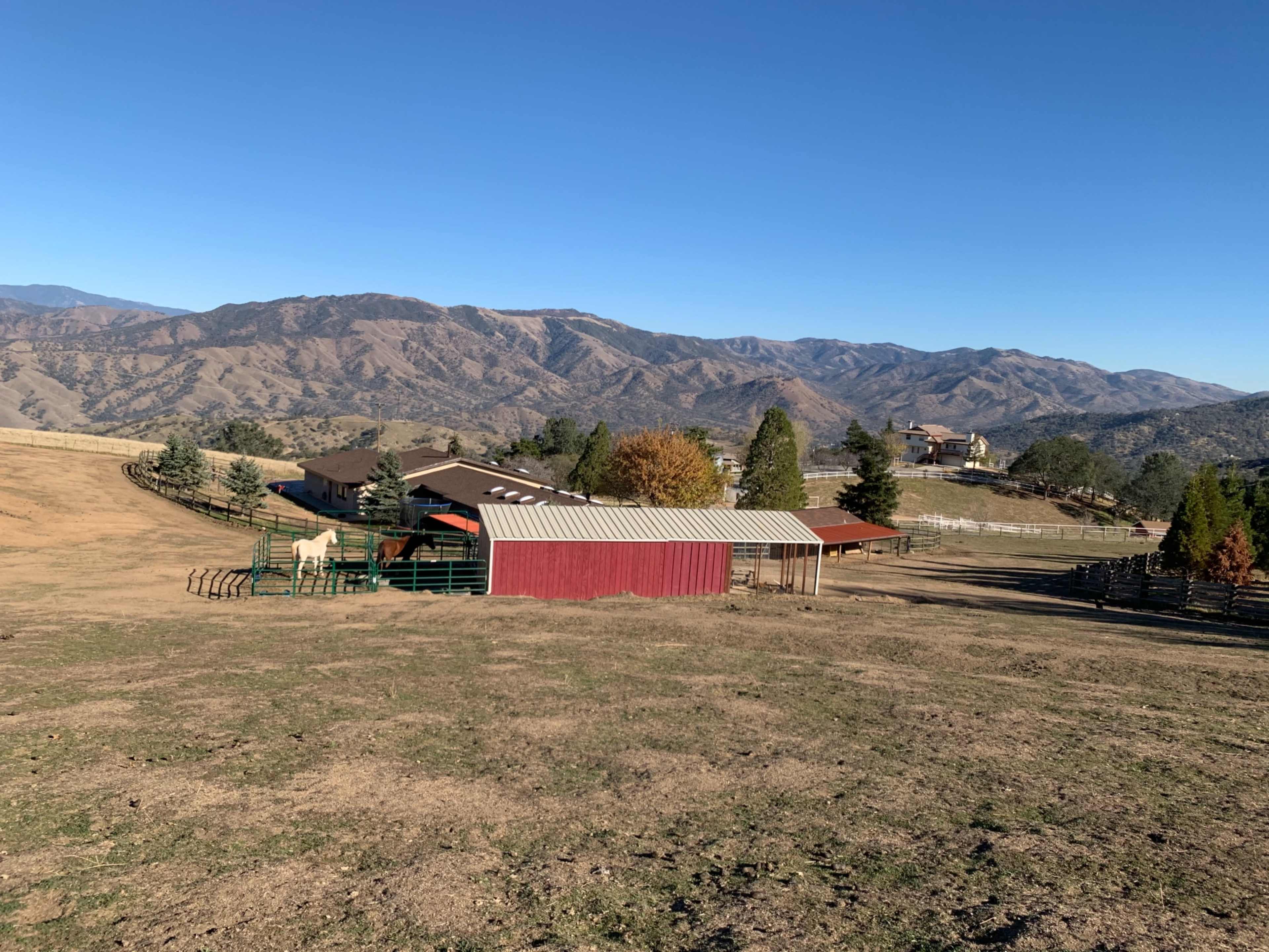 A rural landscape with a red barn, a fenced area, and distant mountains under a clear blue sky.