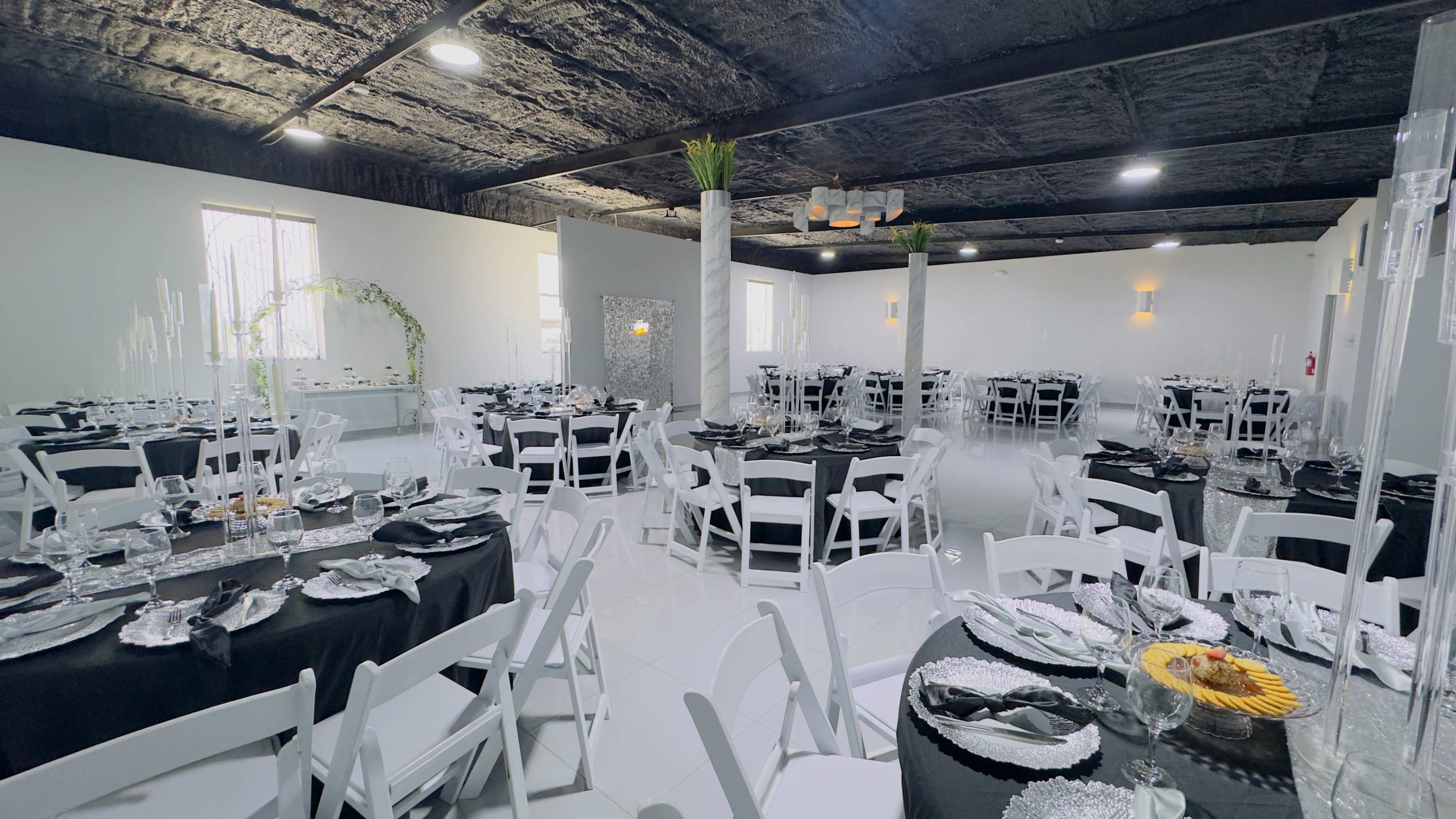 The image shows a banquet hall set up with several round tables, each adorned with black tablecloths and white chairs, arranged neatly for a formal event.