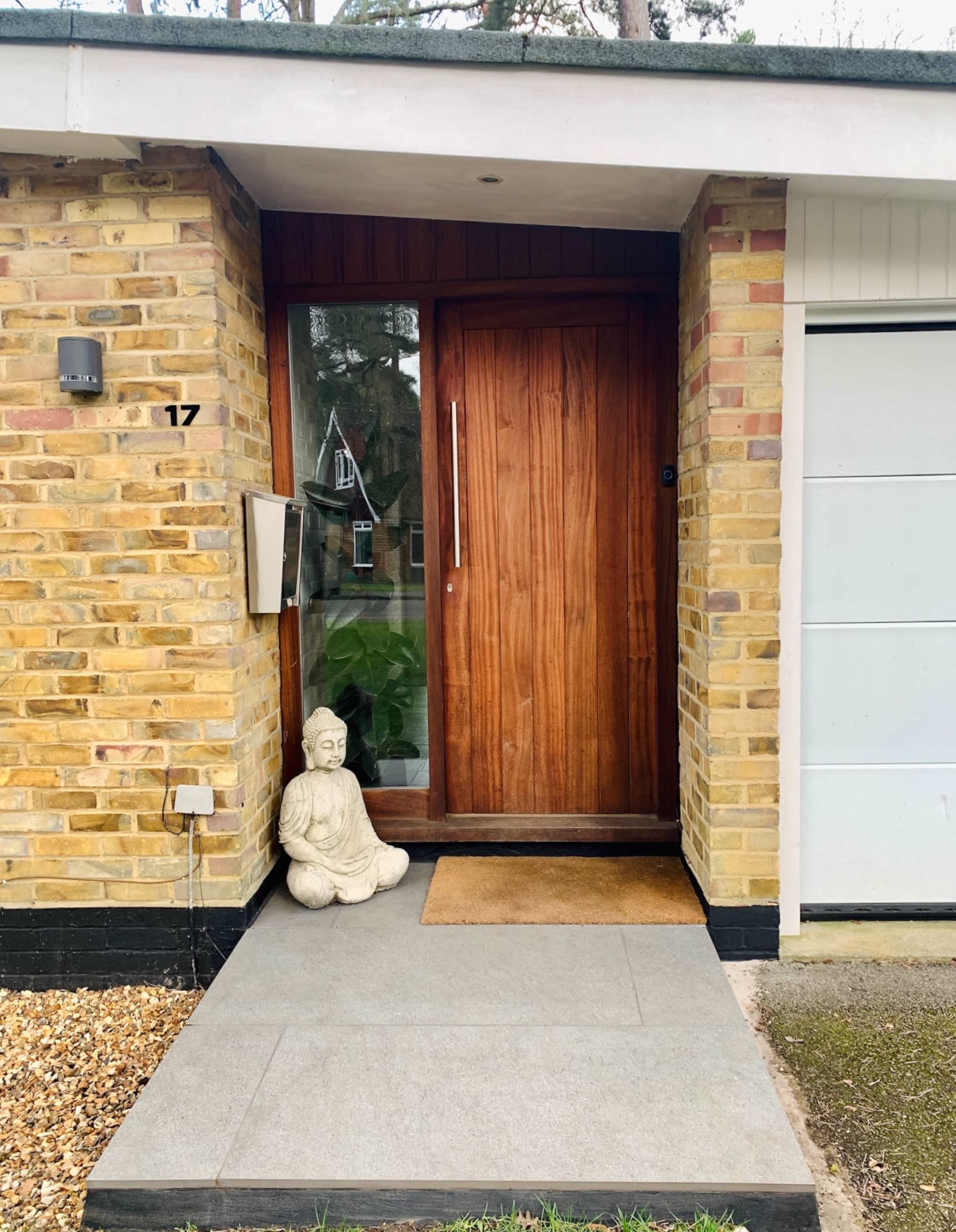 A brick house entrance featuring a wooden door, a statue, and a welcome mat on a stone pathway.