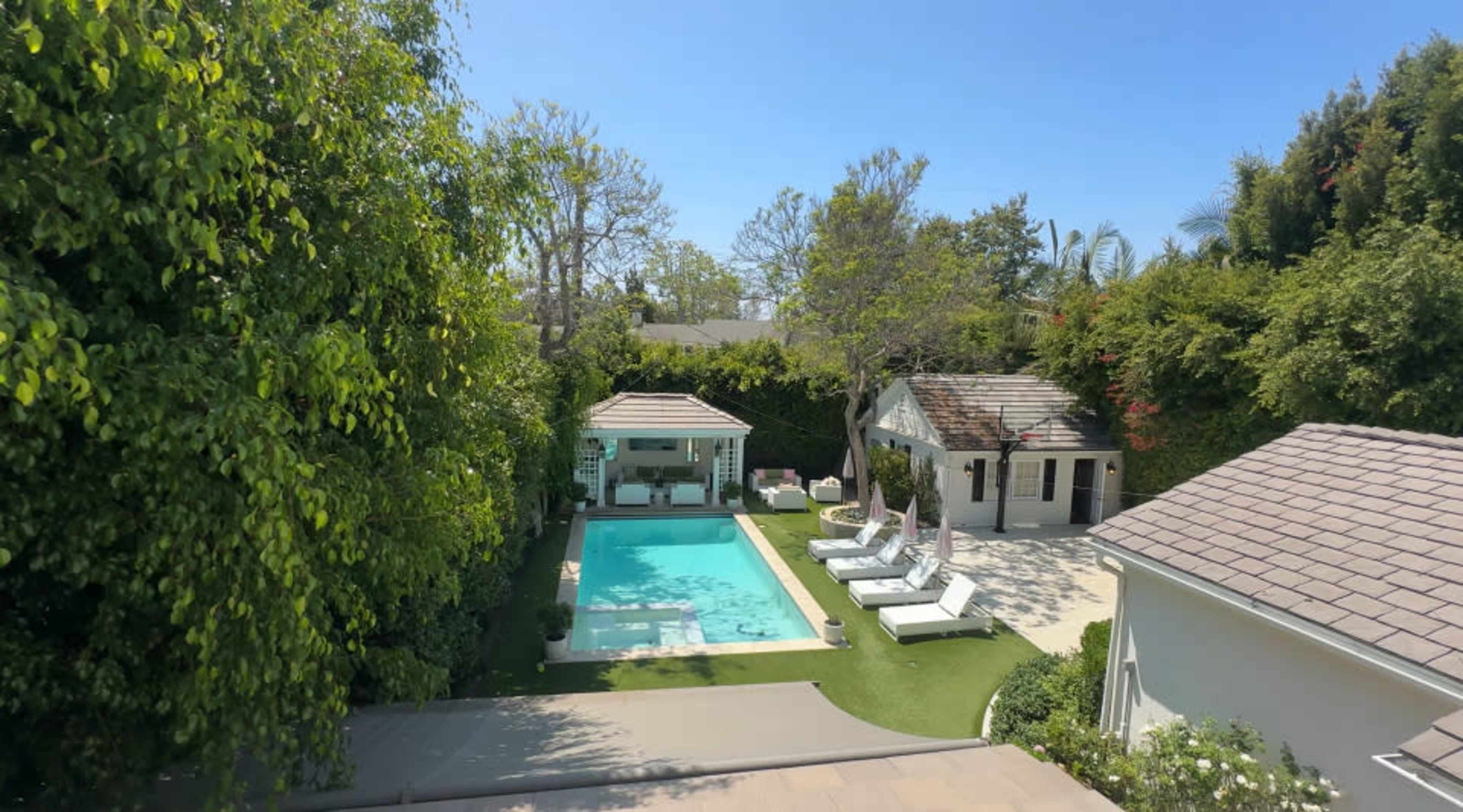 The image shows a residential backyard featuring a swimming pool, several lounge chairs, a gazebo, and landscaped greenery.