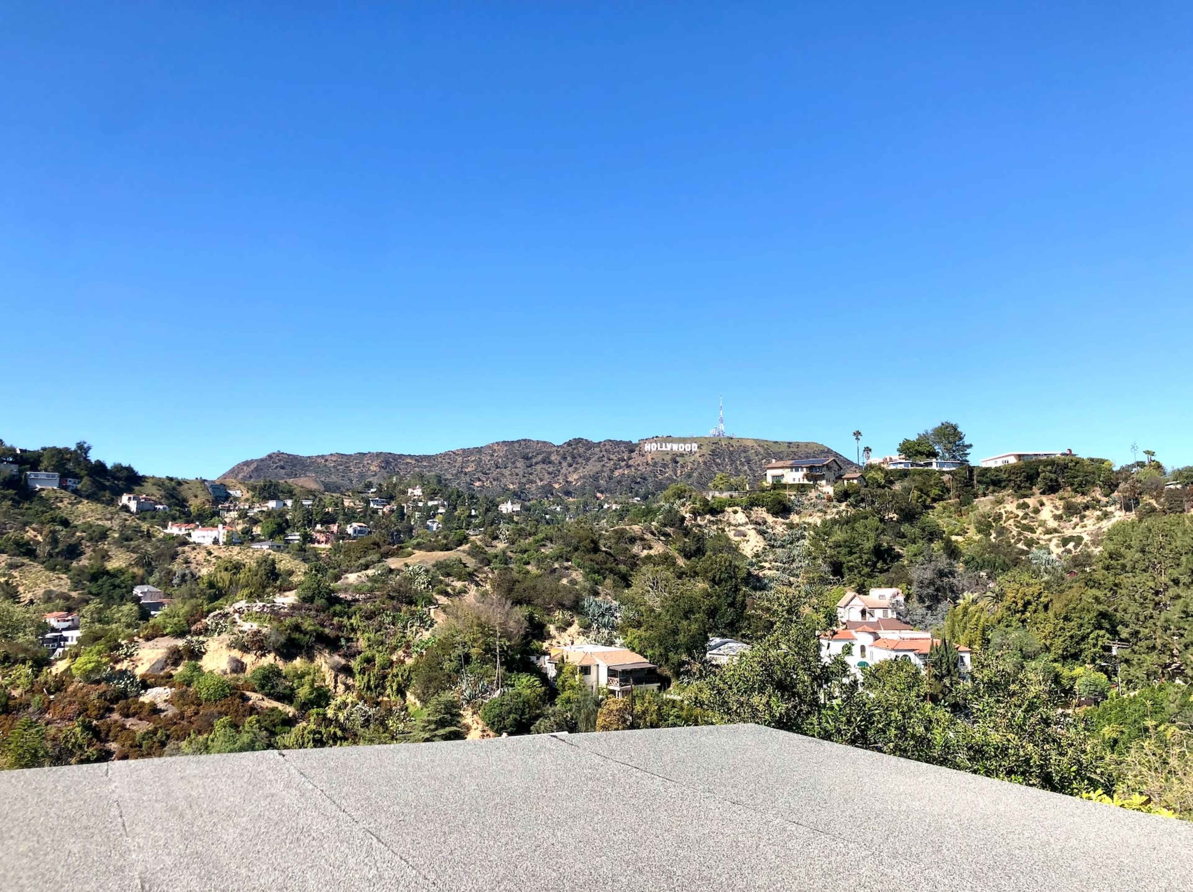 The image shows a clear view of hills and homes, with the Hollywood sign prominently displayed on the mountainside in the background.