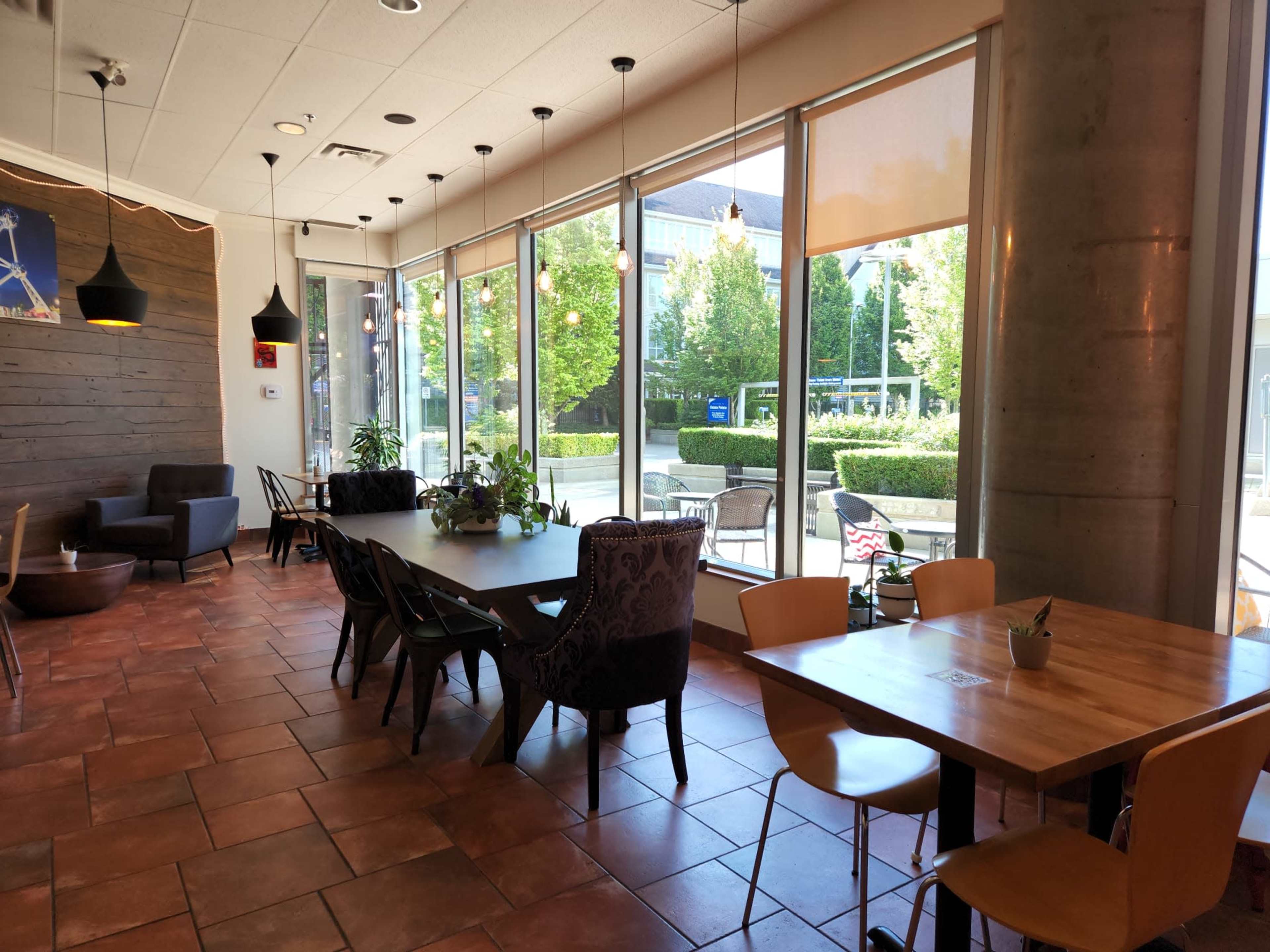 A modern café interior with large windows, natural light, and a mix of seating arrangements, including wooden and upholstered chairs.