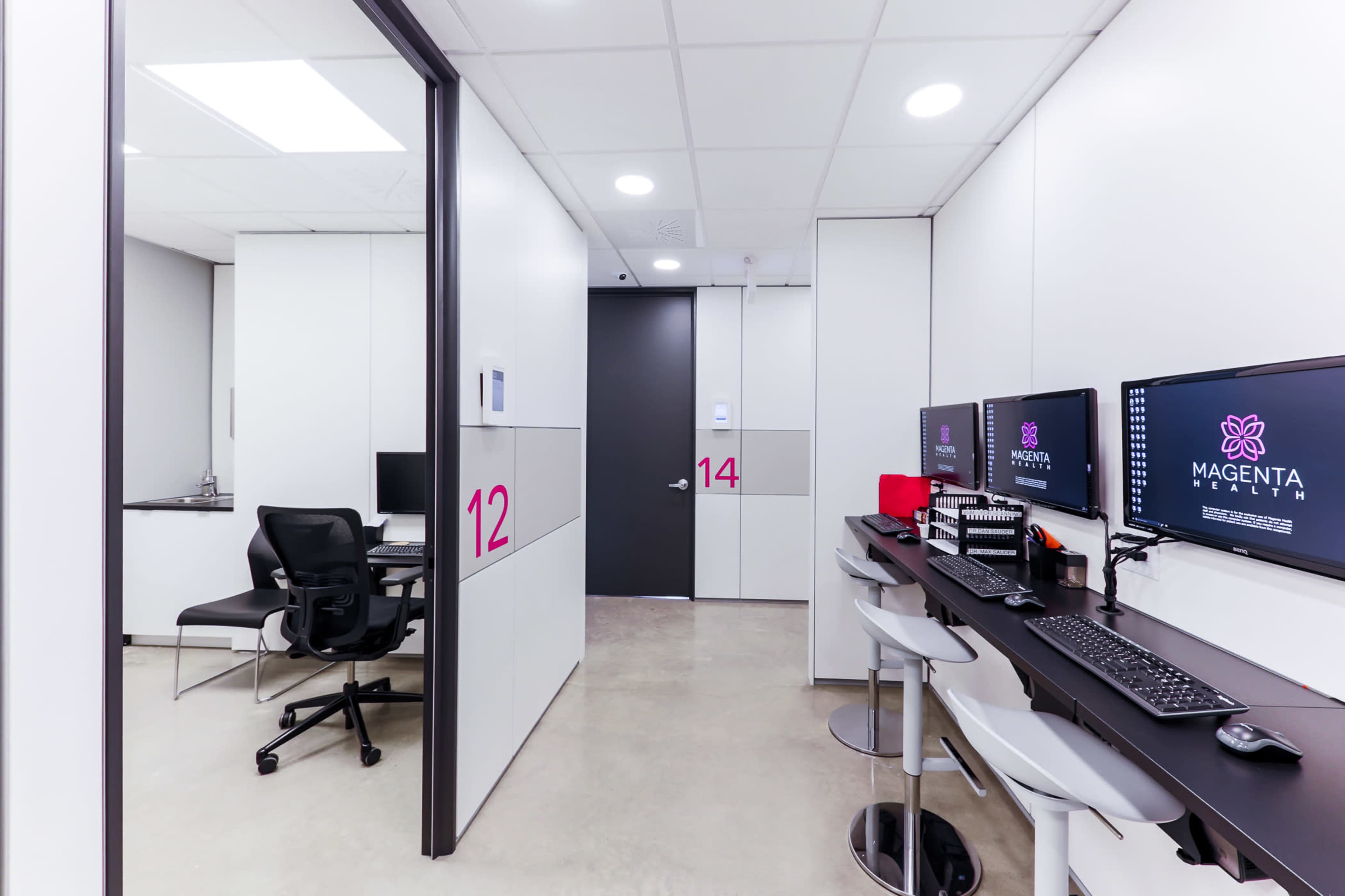 The image shows a modern office space featuring two workstations with computers, a doorway labeled "12," and a door leading to another room marked "14."