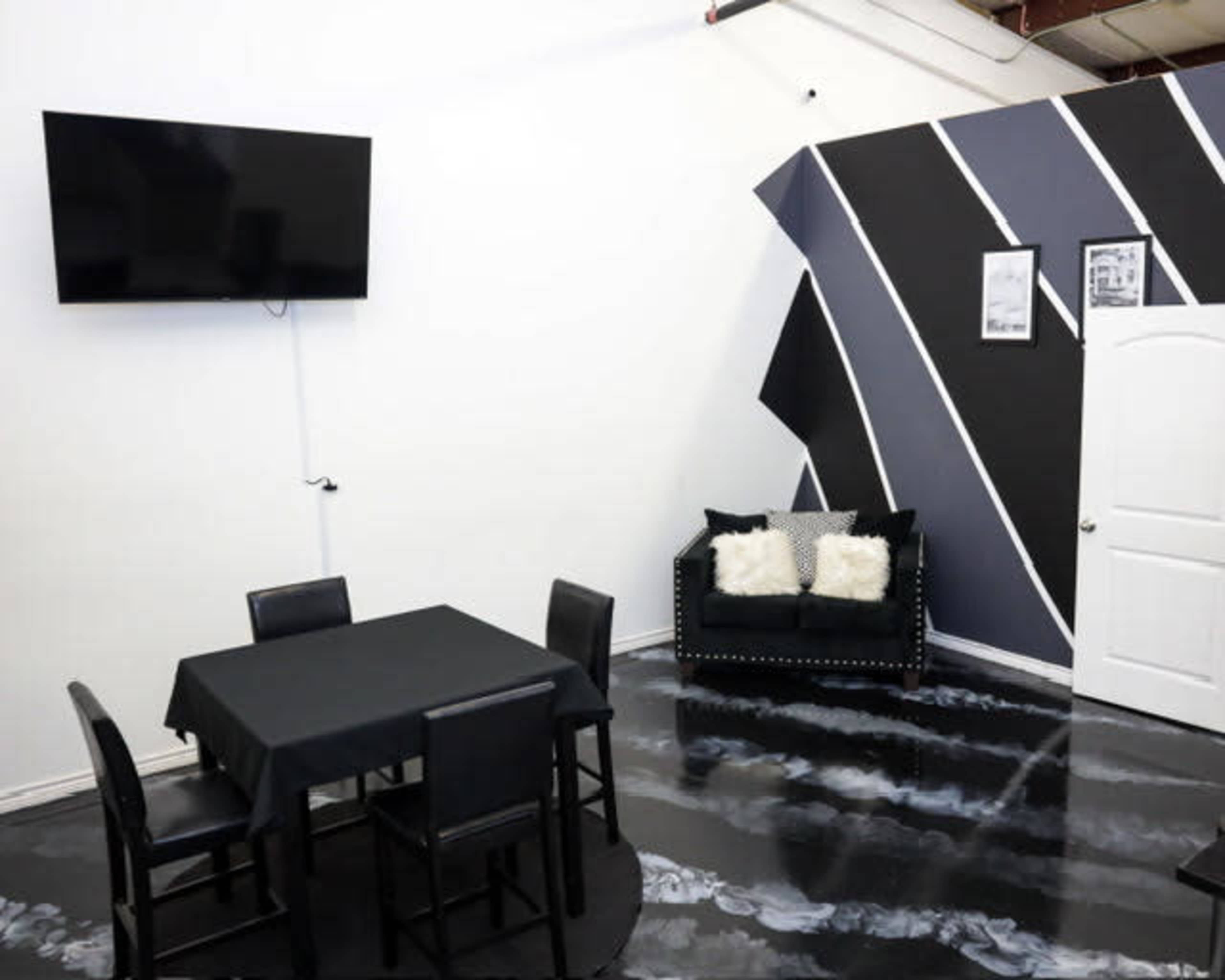 A modern room with a square black table and four chairs, a couch with cushions, a mounted television, and a painted accent wall featuring diagonal black and gray stripes.