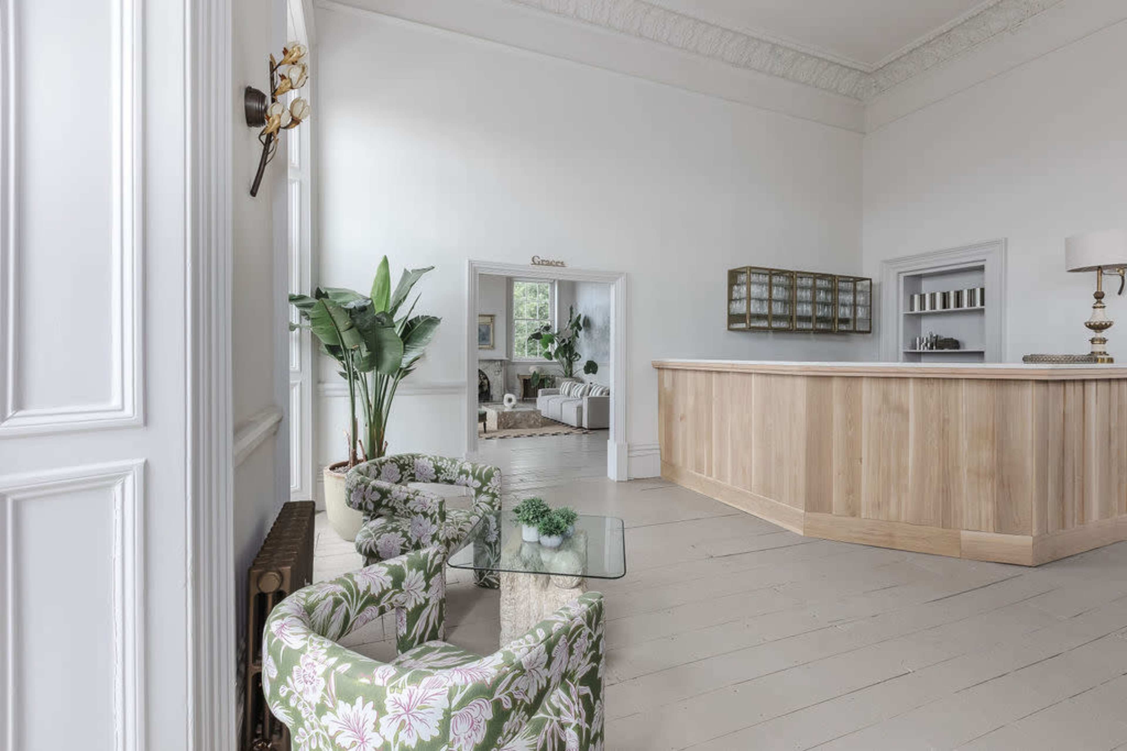 A bright, spacious reception area featuring floral-patterned chairs, a wooden reception desk, and large windows with plants.