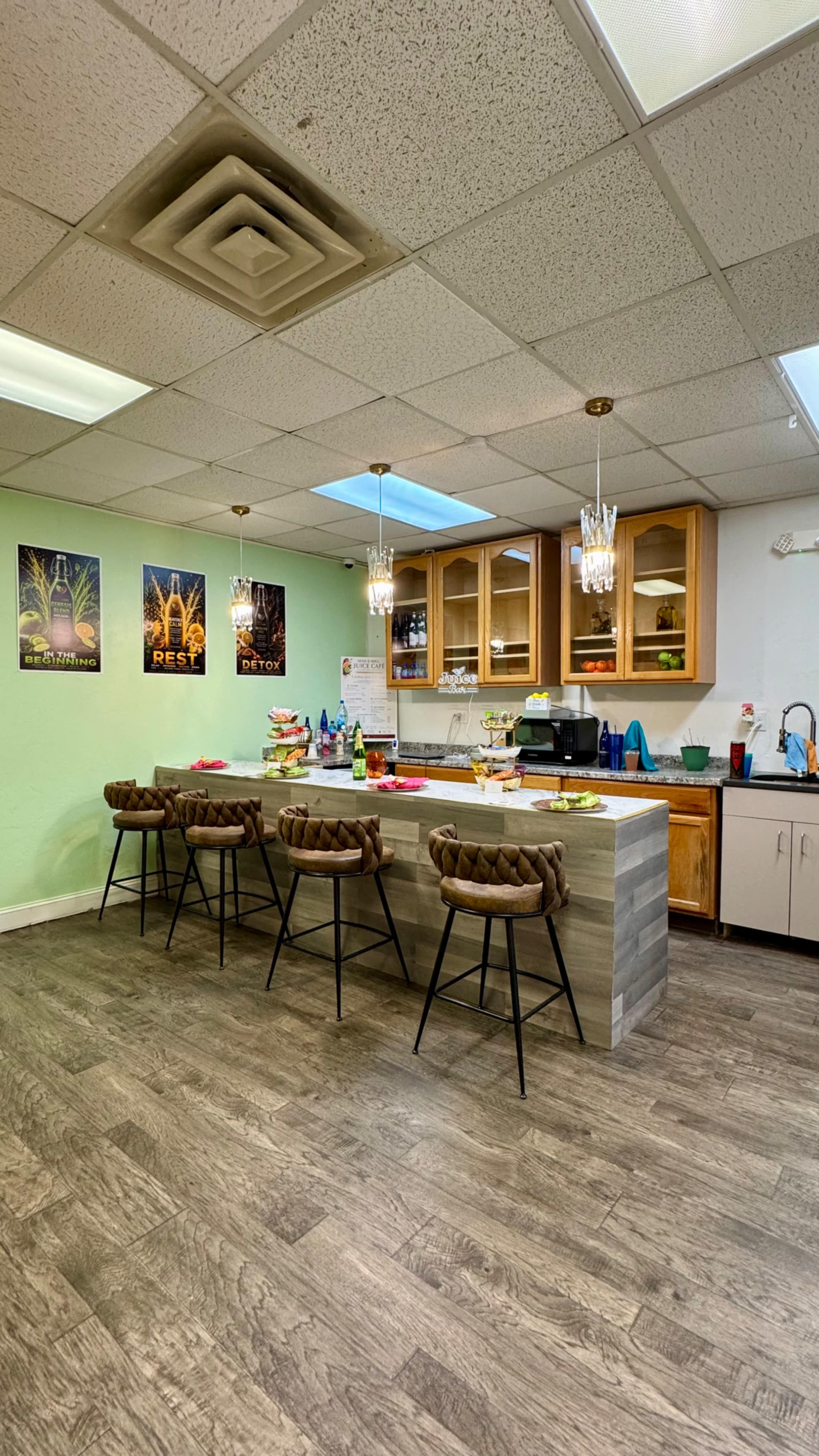 The image shows a kitchen area with four barstools at a counter, cabinets with dishes, and various food items displayed on the counter and shelves.