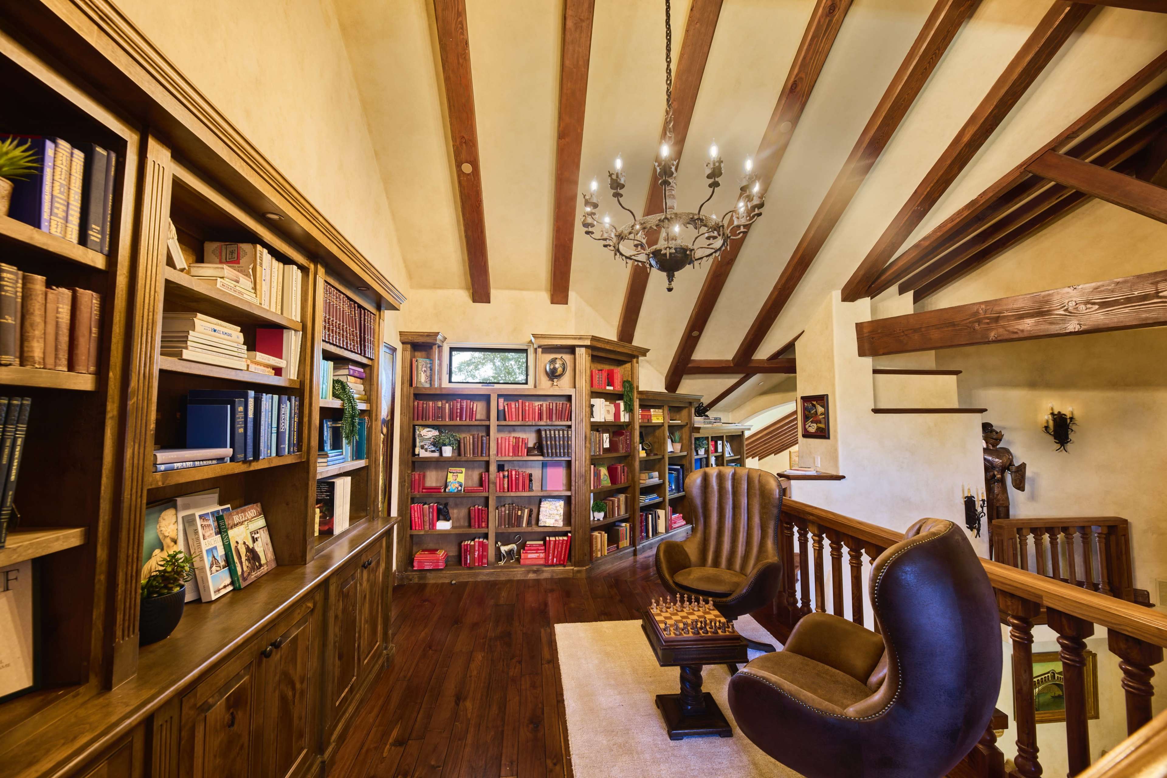 A well-appointed library with wooden shelves filled with books and cozy seating, illuminated by a chandelier.