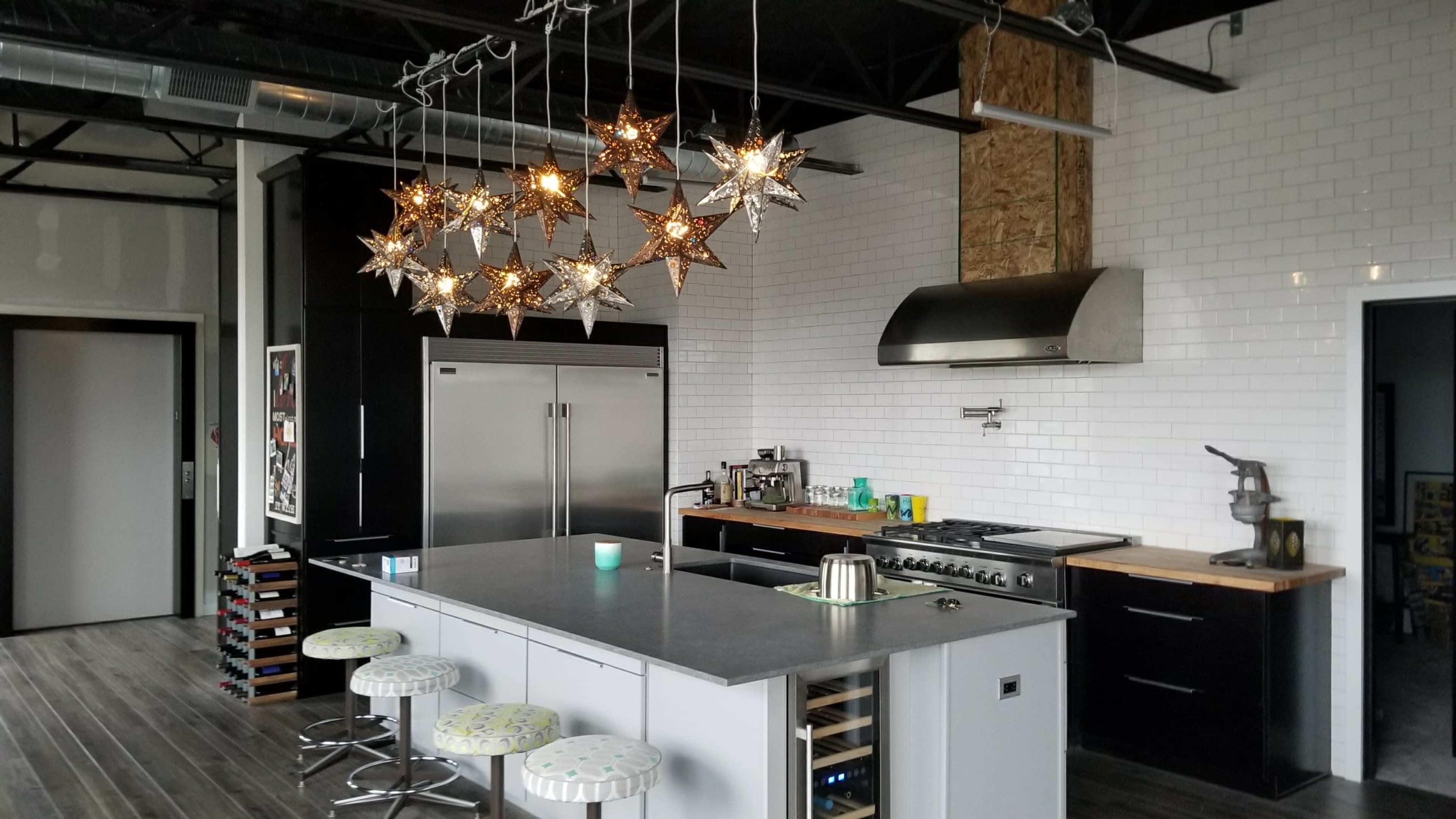 The kitchen features a centrally located island with stools, surrounded by black cabinetry and hanging star-shaped lights.