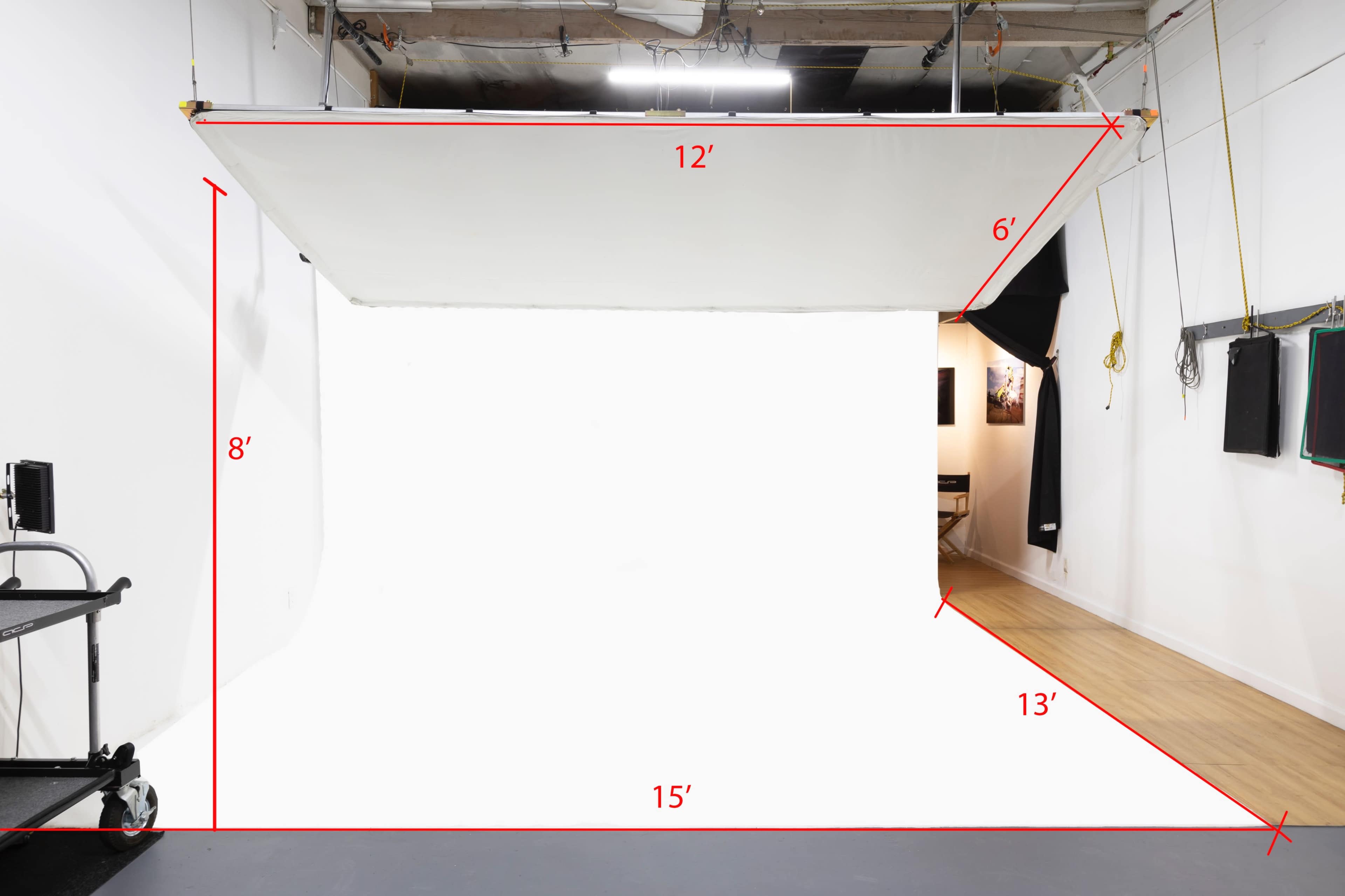A photography studio with a large, white backdrop measuring 12 feet by 6 feet, suspended from the ceiling in a space measuring approximately 15 feet by 13 feet.