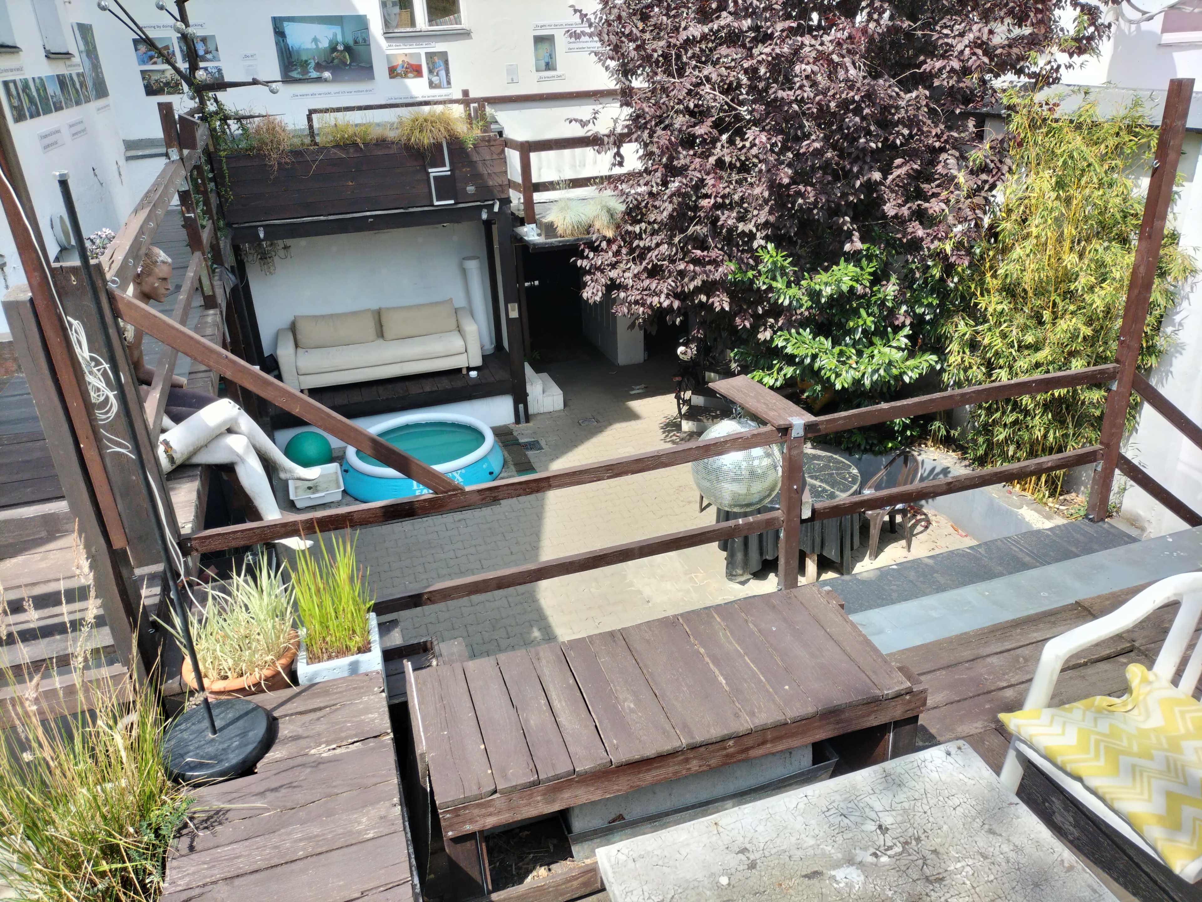 A rooftop terrace with wooden decking, a small pool, a seating area, and various potted plants.