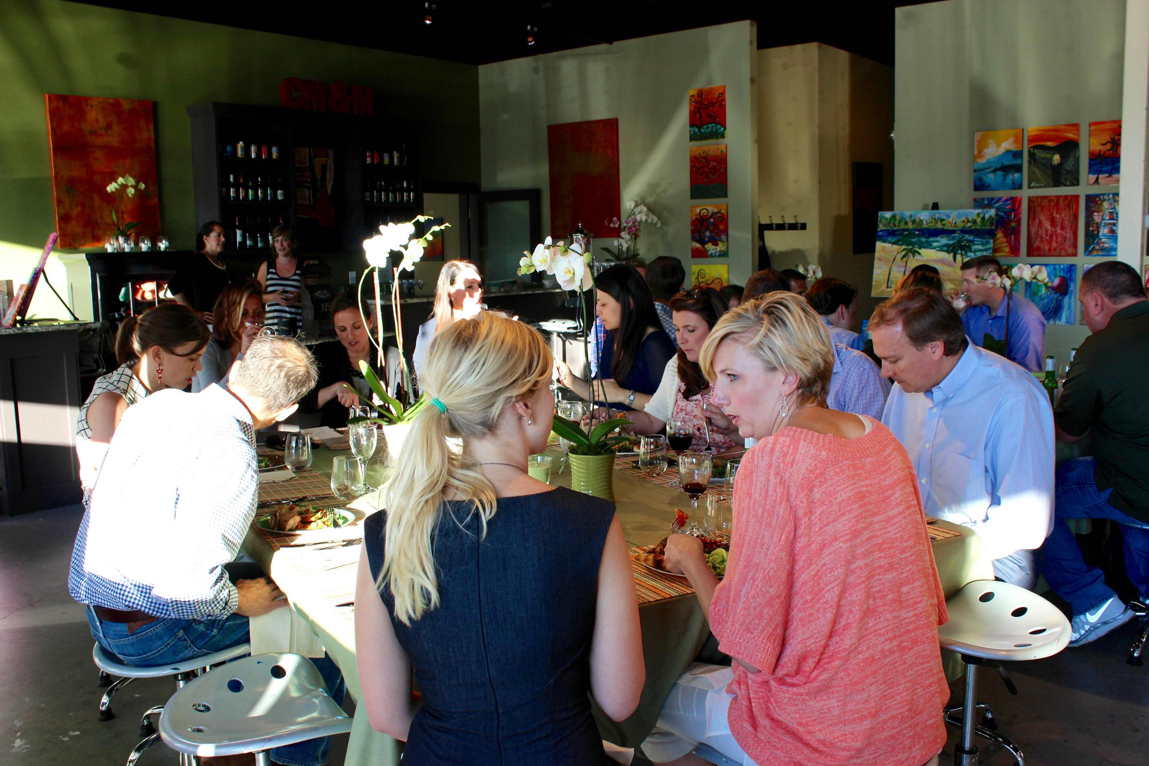 A group of people is seated around a long table in a well-decorated restaurant, enjoying a meal and engaging in conversation.