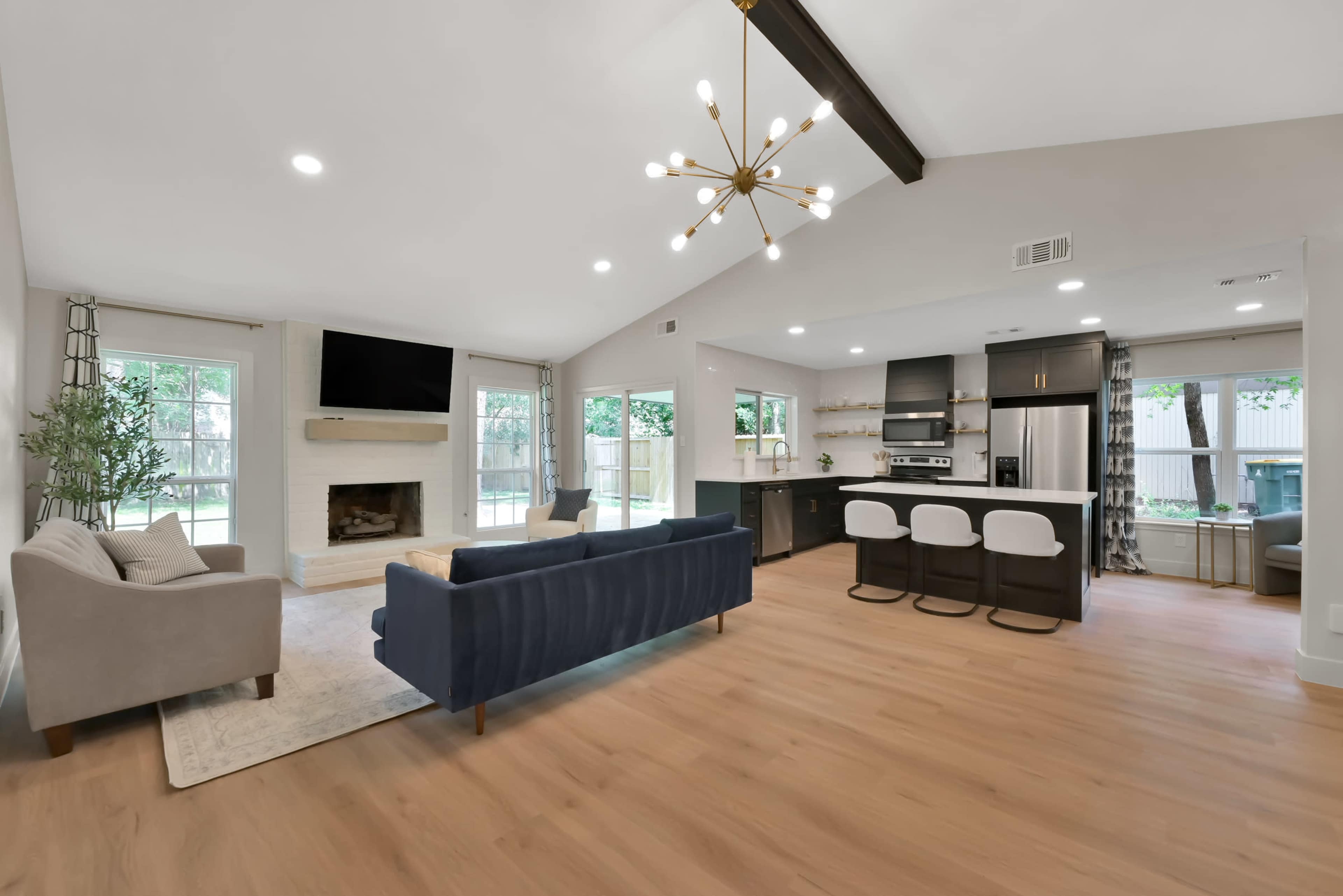A spacious living area with a fireplace, modern kitchen, and seating arrangements, featuring large windows that provide natural light.